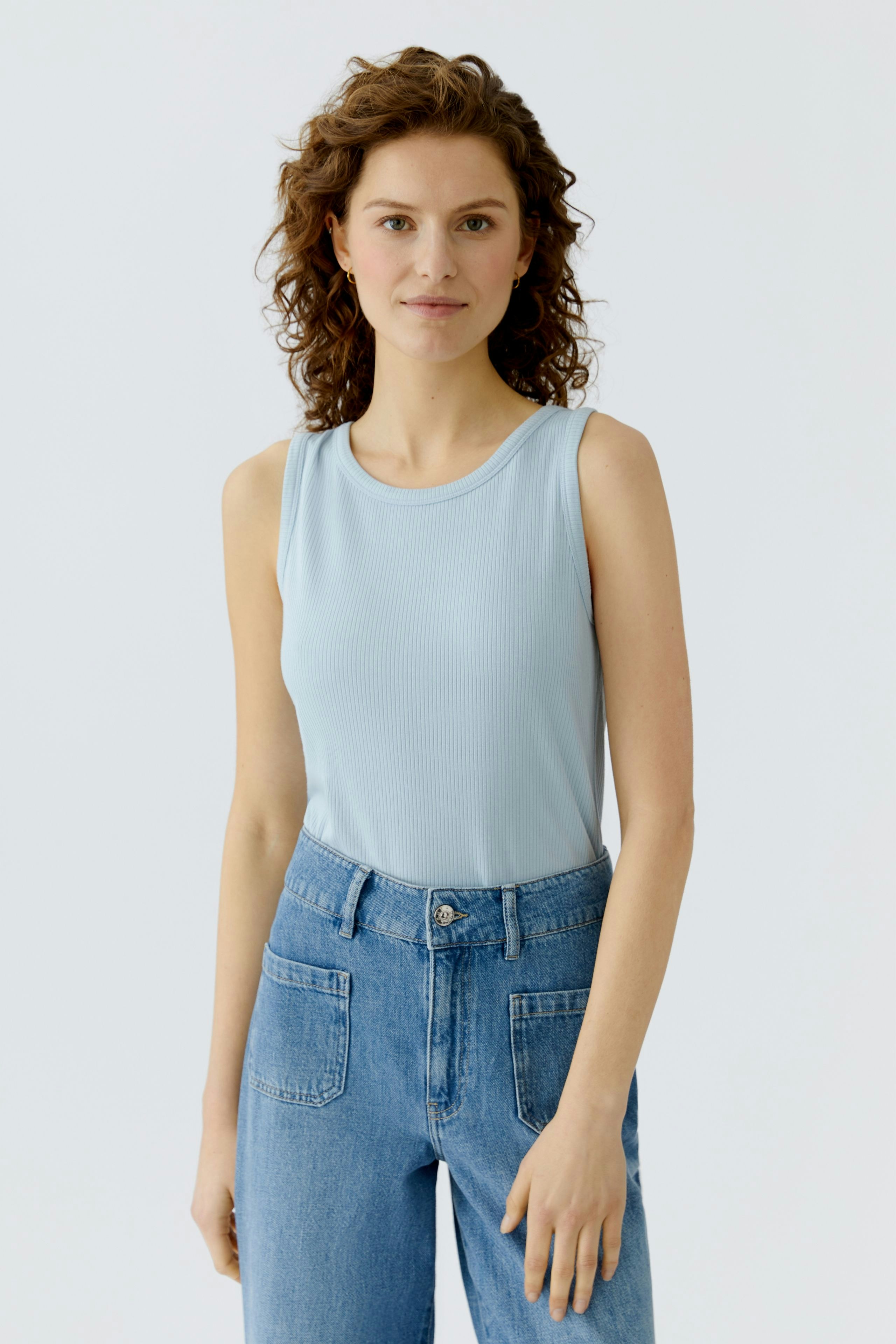 Light blue top: Woman in a sleeveless top paired with high-waisted jeans, showcasing a casual style.