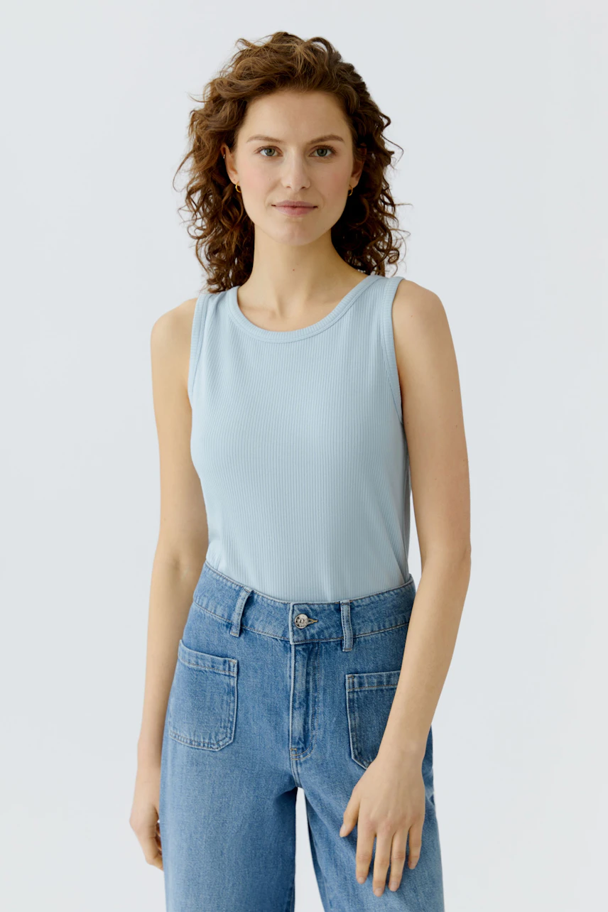 Light blue top: Woman in a sleeveless top paired with high-waisted jeans, showcasing a casual style.
