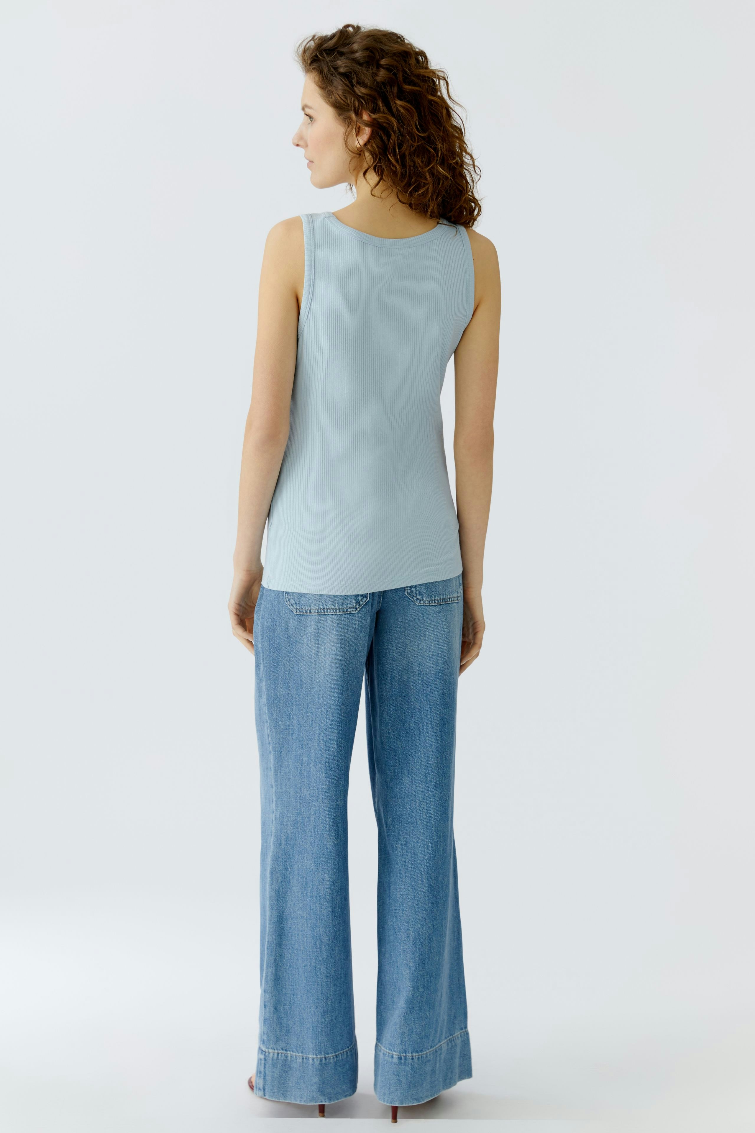 Casual women's top: Young woman in a light blue sleeveless top and wide-leg jeans, seen from the back.