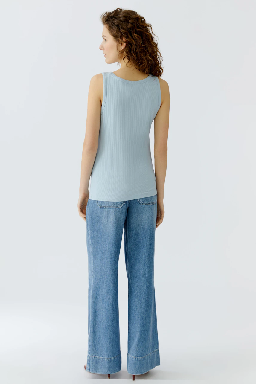 Casual women's top: Young woman in a light blue sleeveless top and wide-leg jeans, seen from the back.