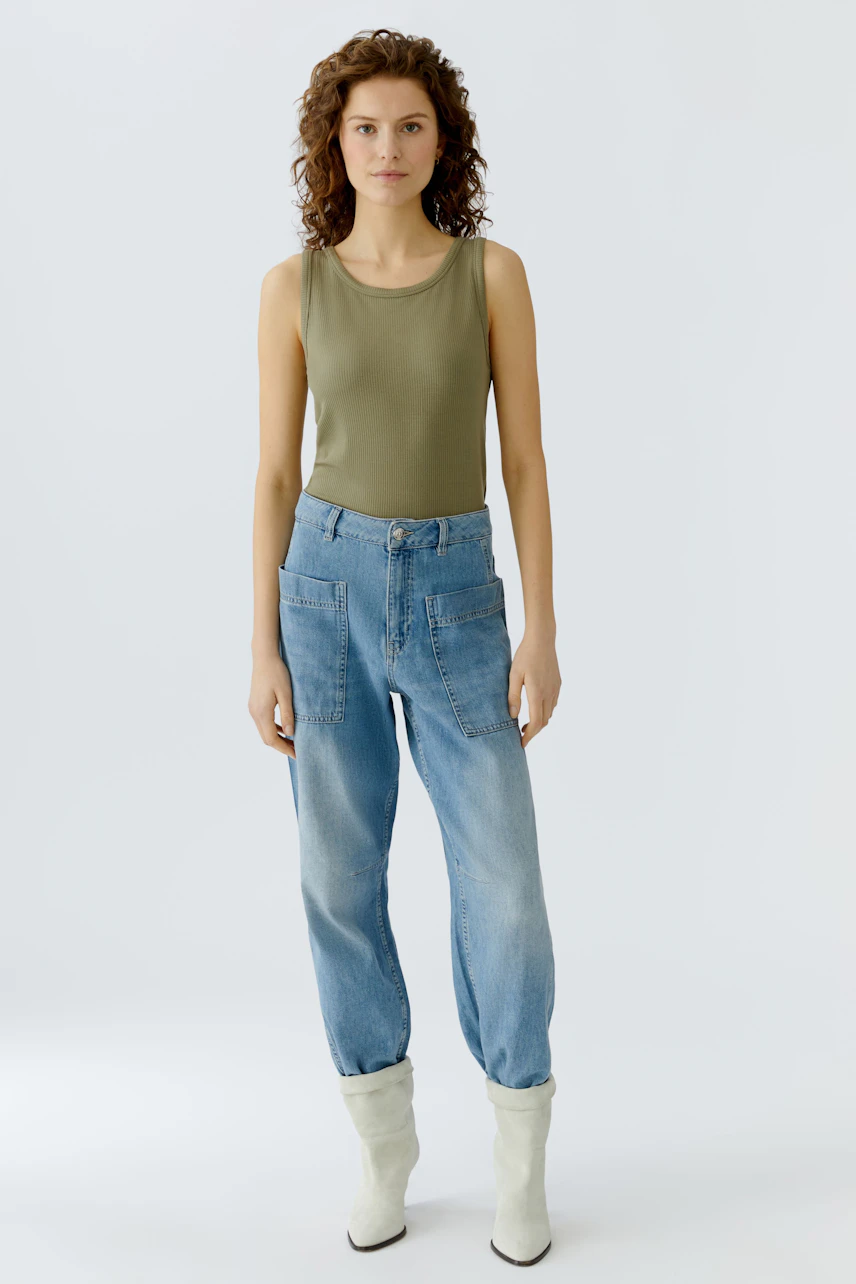 Damen-Top: Junge Frau in einem olivgrünen ärmellosen Top und lässigen Jeans steht entspannt.