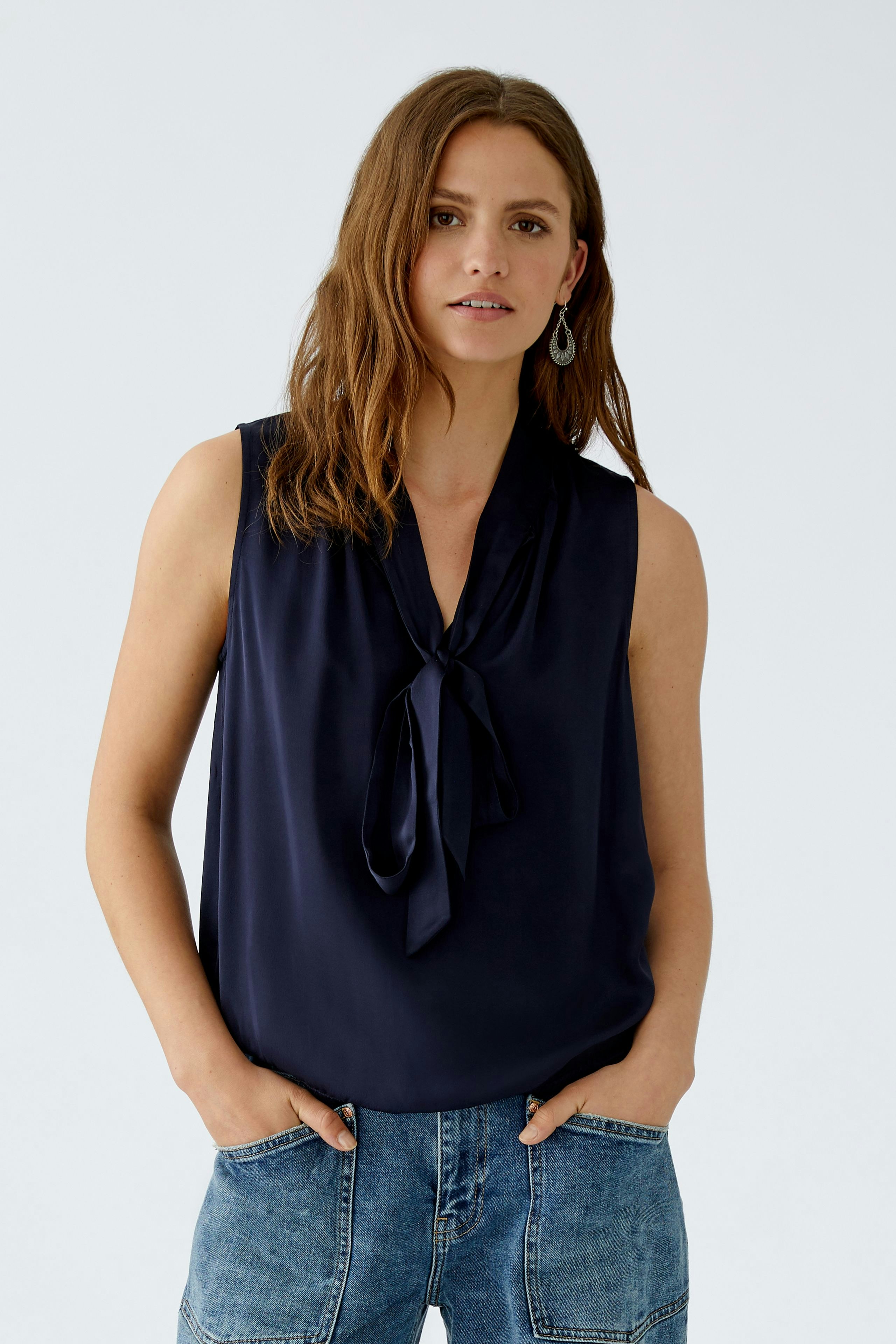 Sleeveless blouse: Woman in a navy top with a tie detail, paired with casual denim.