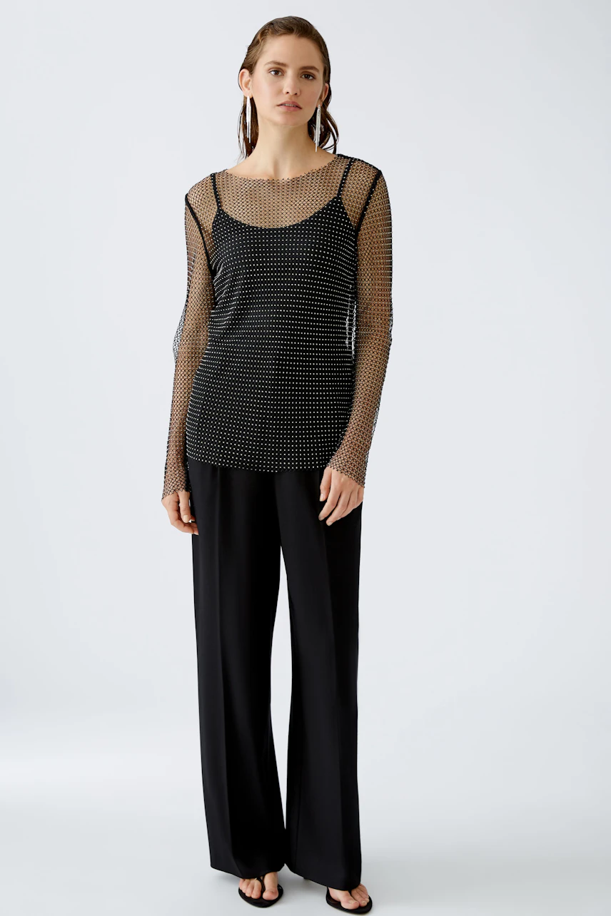 Elegantes Langarmshirt: Frau in schwarzem, transparentem Shirt mit Punkten und lässiger Hose.