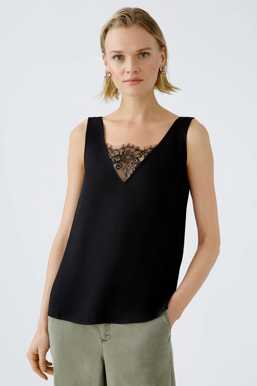 Elegant women's top: A woman in a black sleeveless top with lace detail, exuding sophistication.