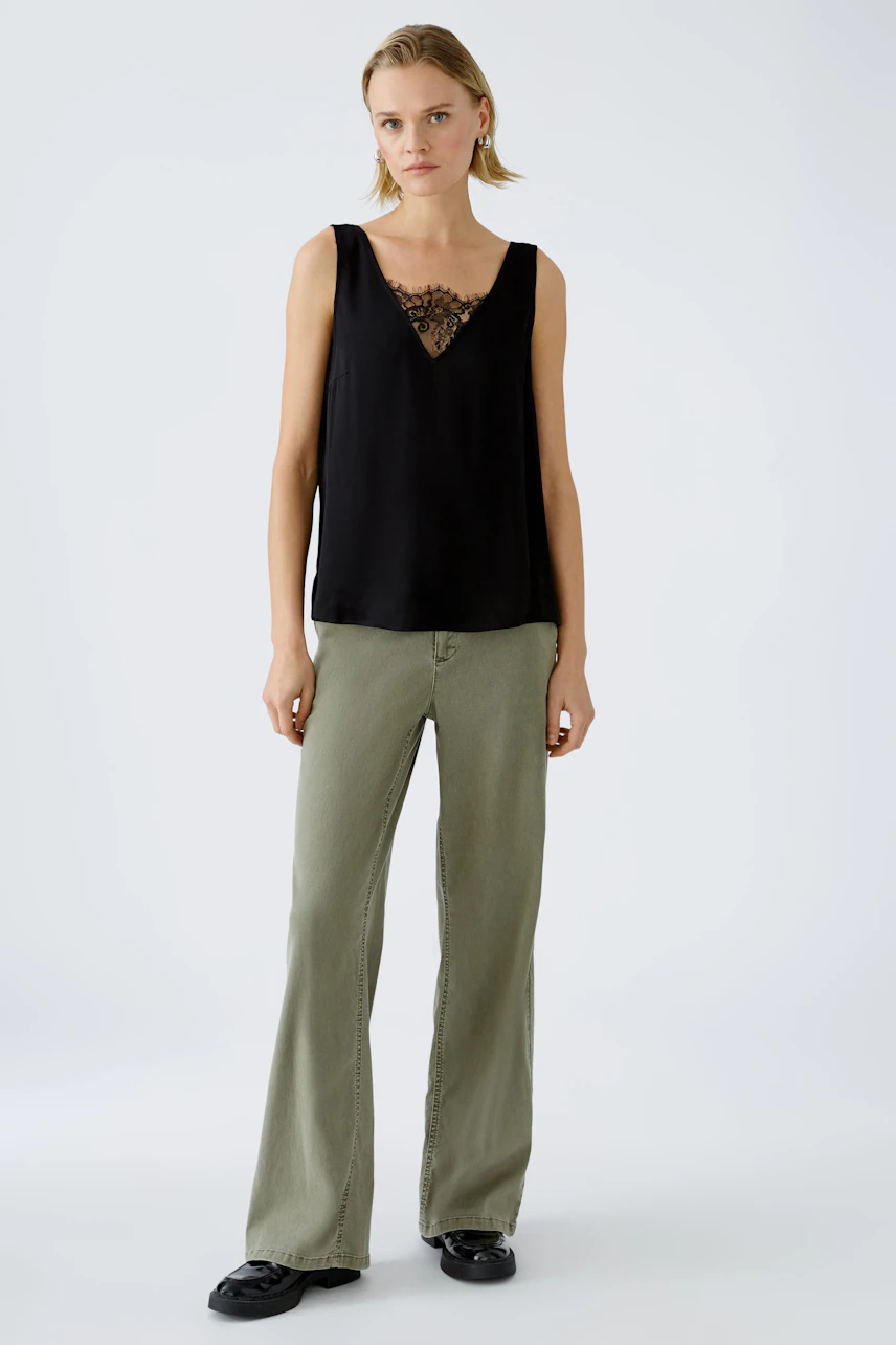 Elegant women's top: A woman in a black sleeveless top with lace detail, paired with relaxed-fit pants.
