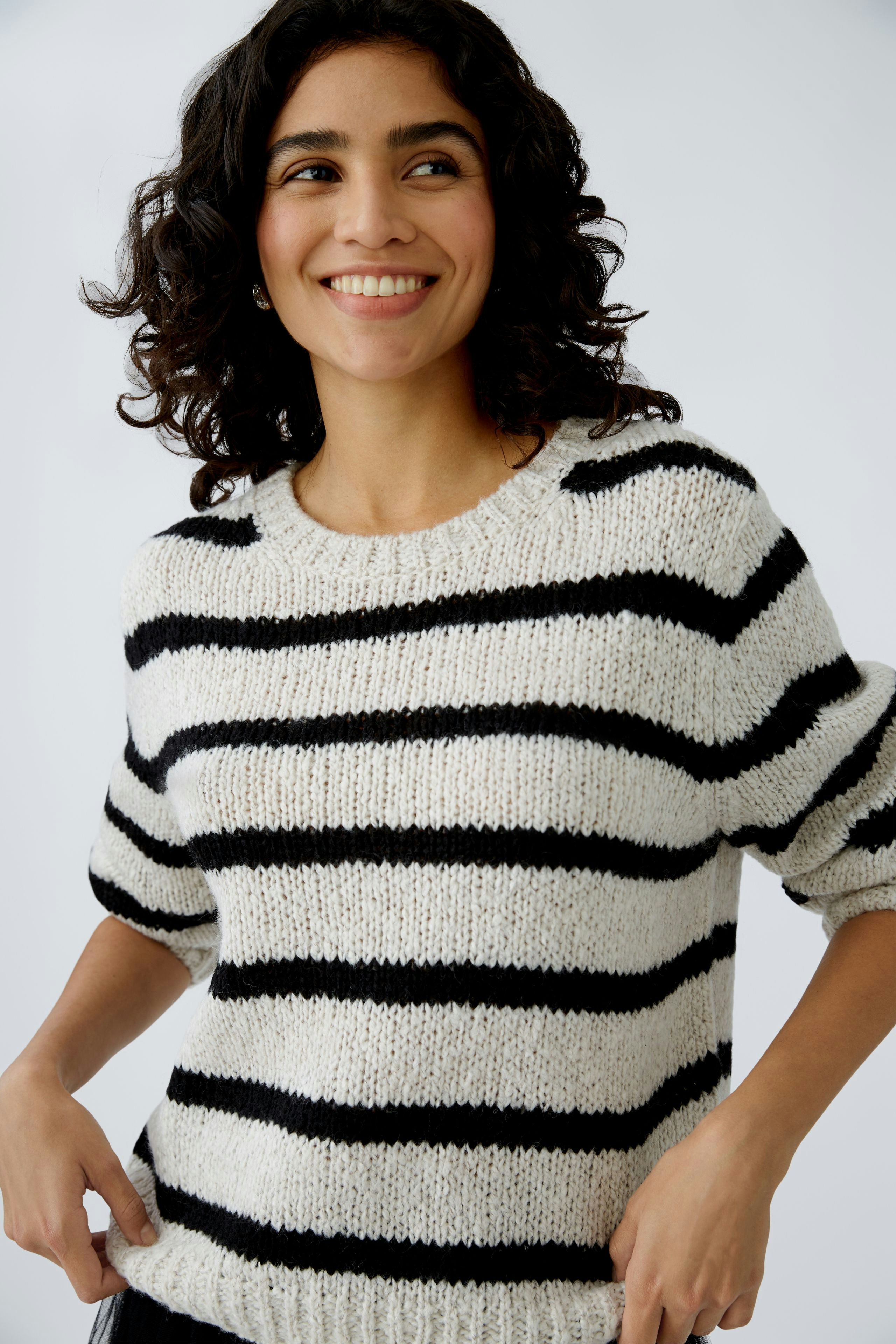 Stylish women's pullover: A woman smiles in a cozy striped pullover with black and white lines.