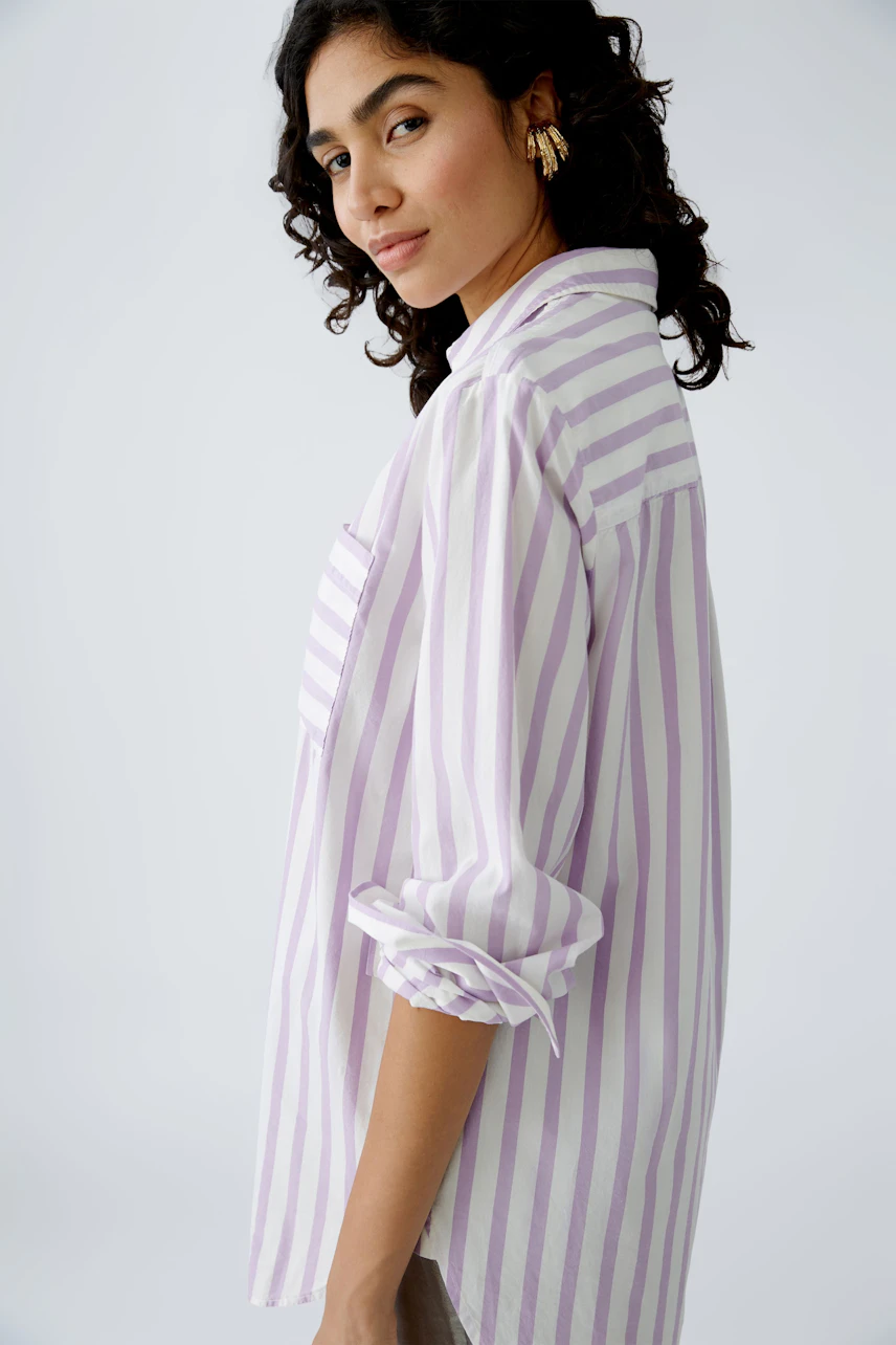 Stylish women's blouse: A woman in a light purple striped blouse with rolled-up sleeves.