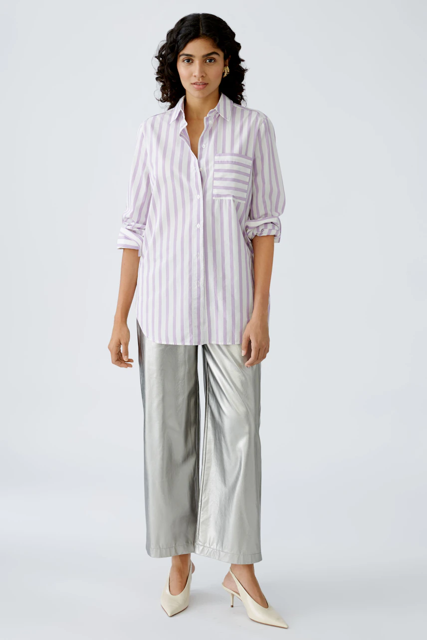 Stylish women's blouse: A woman in a striped shirt with a pocket, paired with shiny silver pants.