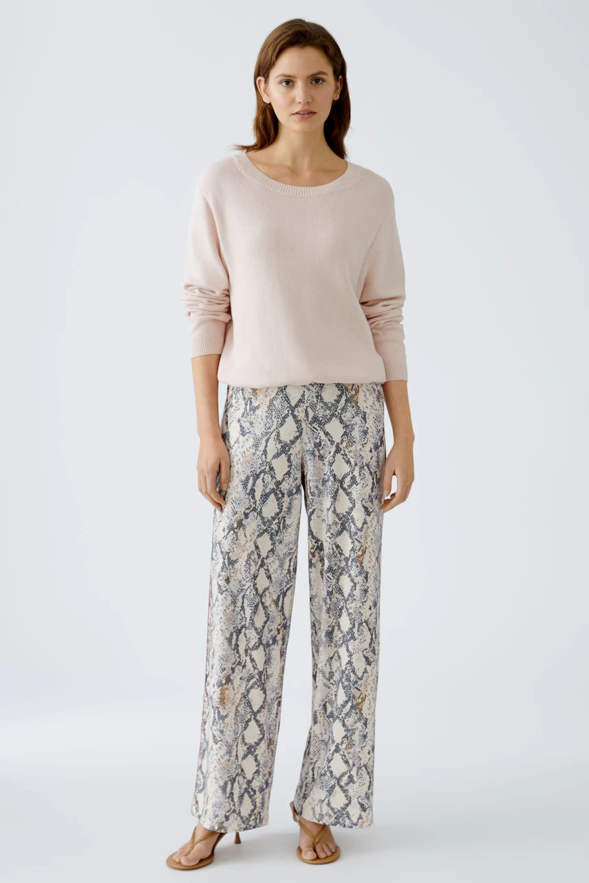 Stylish women's pullover in soft pink, paired with trendy snake-print pants for a chic look.
