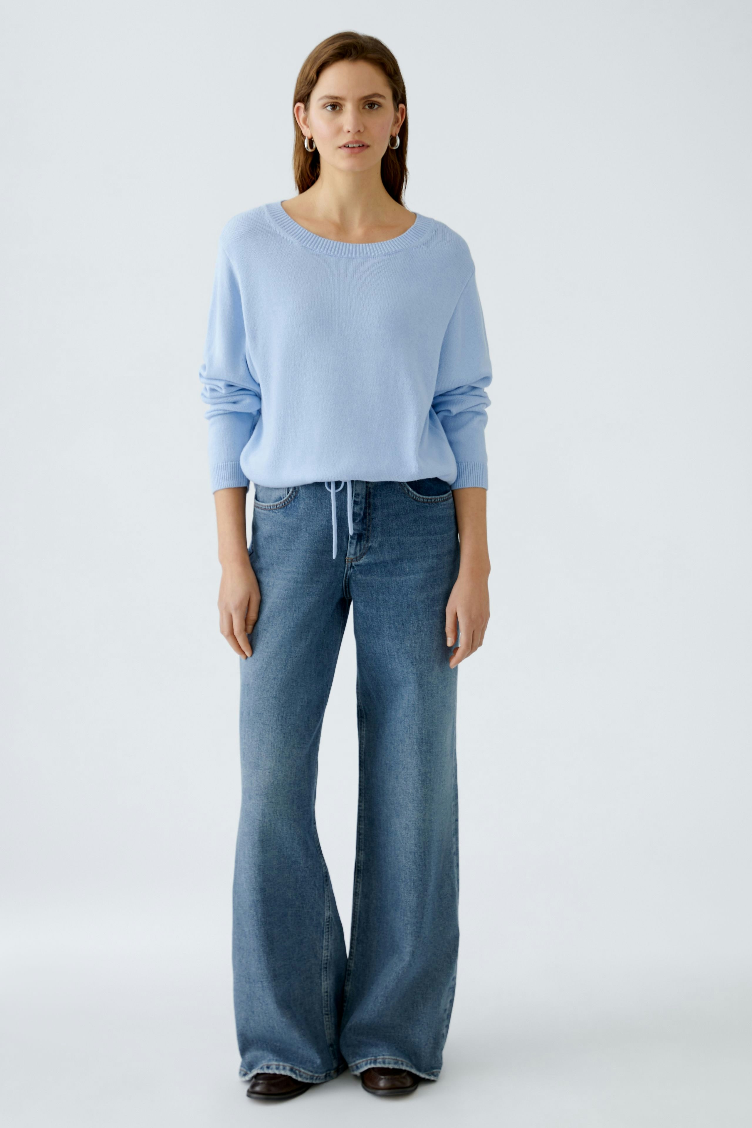 Damen-Pullover: Frau in hellblauem, lässigem Strickpullover mit weiten Jeans.