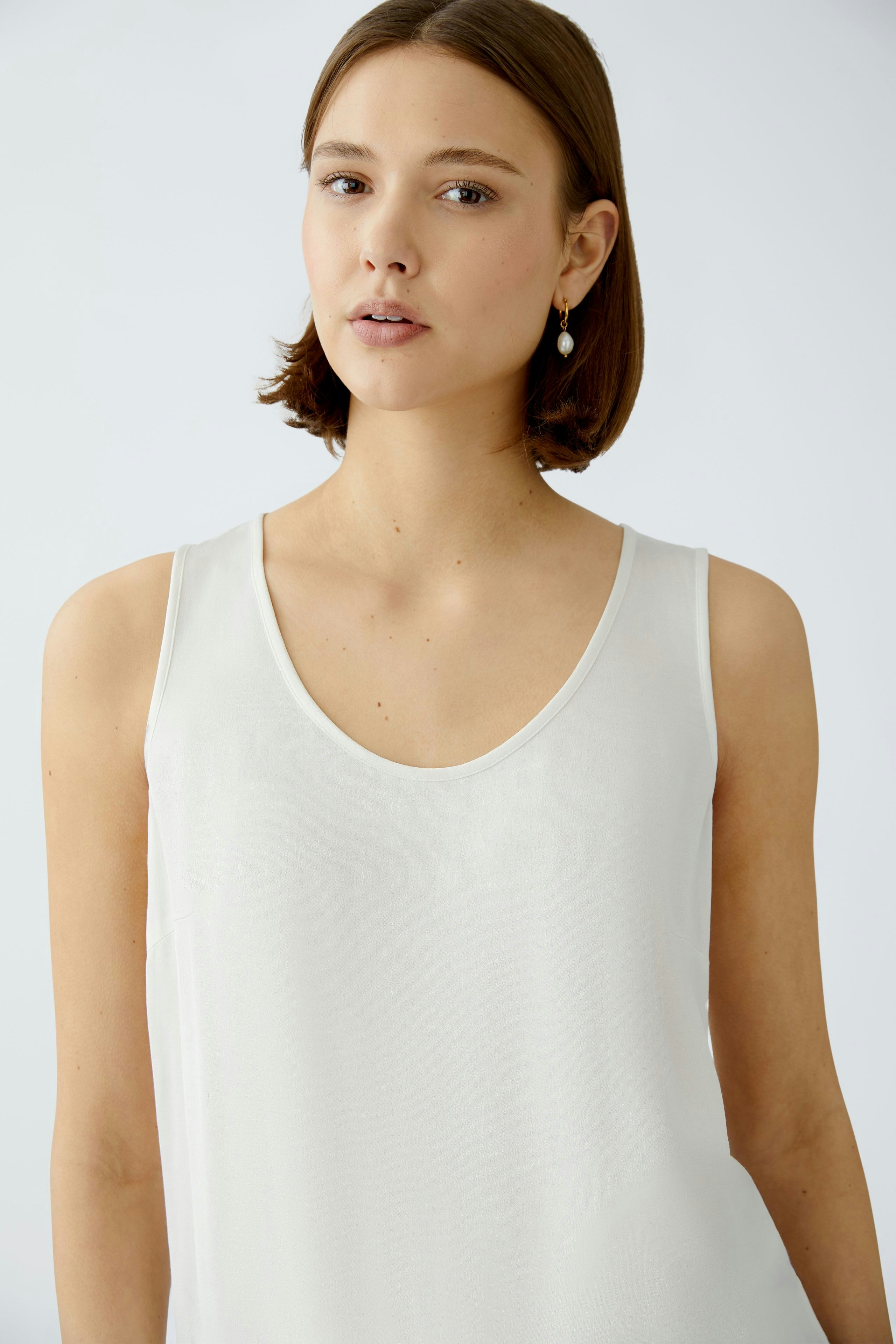 Elegant women's top: A woman in a light, sleeveless top with a deep neckline, exuding effortless style.