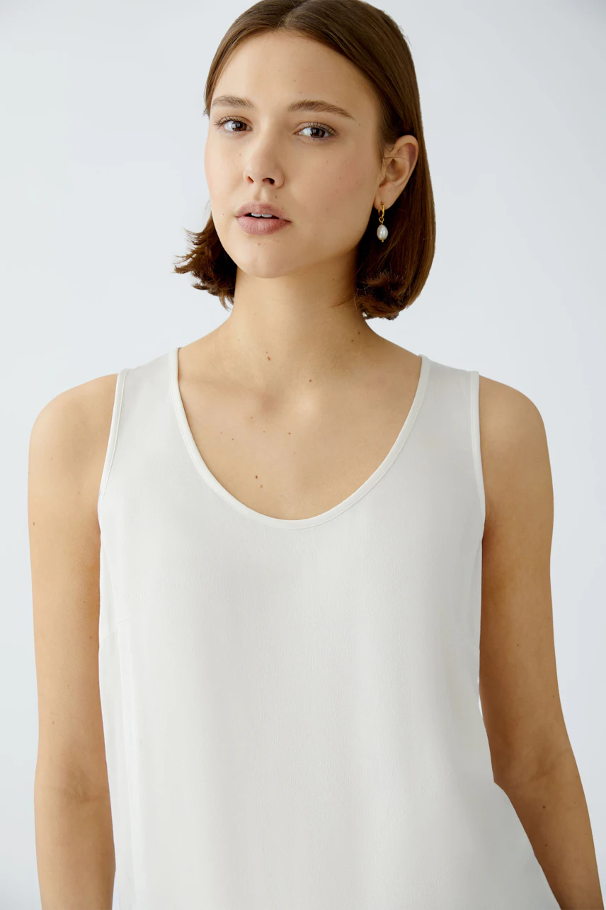 Elegant women's top: A woman in a light, sleeveless top with a deep neckline, exuding effortless style.