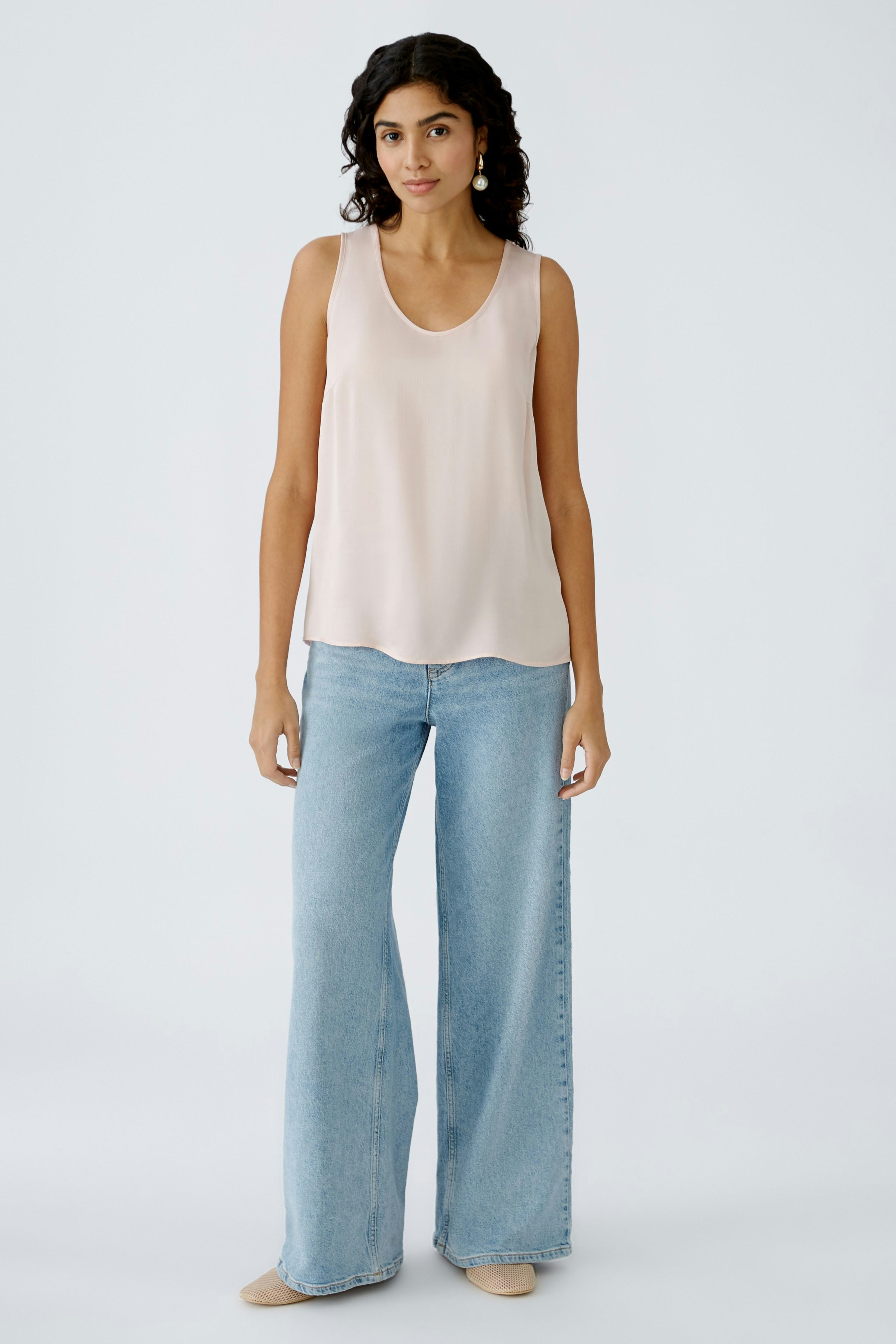 Elegant women's top: A woman in a light pink sleeveless top paired with wide-leg jeans.