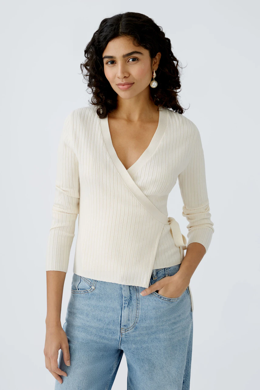 Elegant women's cardigan: A woman in a cream ribbed wrap cardigan paired with casual jeans.