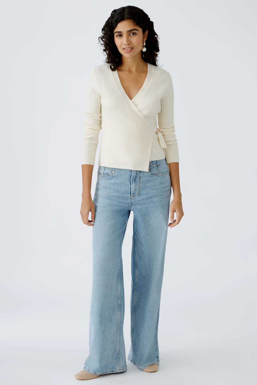 Elegant women's cardigan: A woman in a cream wrap cardigan paired with light blue jeans.