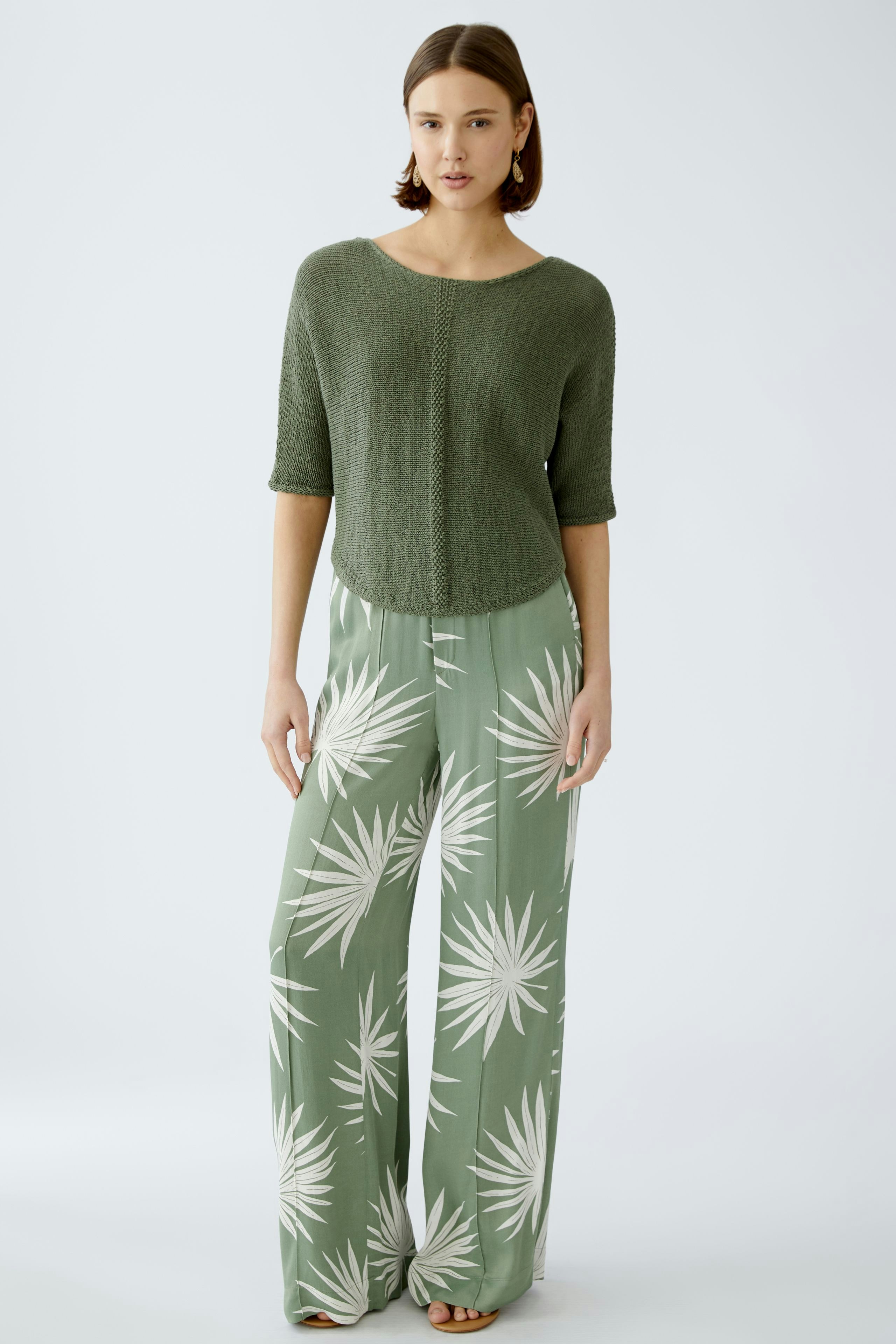 Stylish women's pullover: A woman in a green knitted pullover paired with flowy patterned pants.