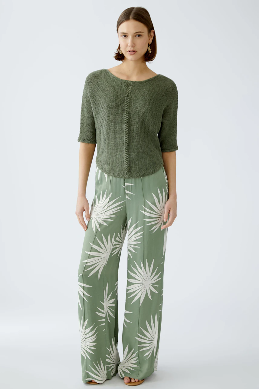 Stylish women's pullover: A woman in a green knitted pullover paired with flowy patterned pants.