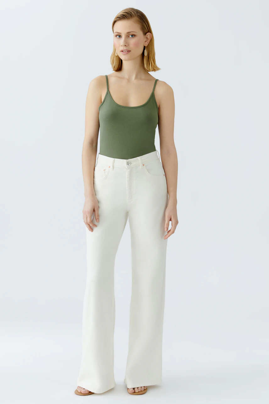Stylish women's top: A woman in a green tank top paired with white wide-leg pants stands confidently.