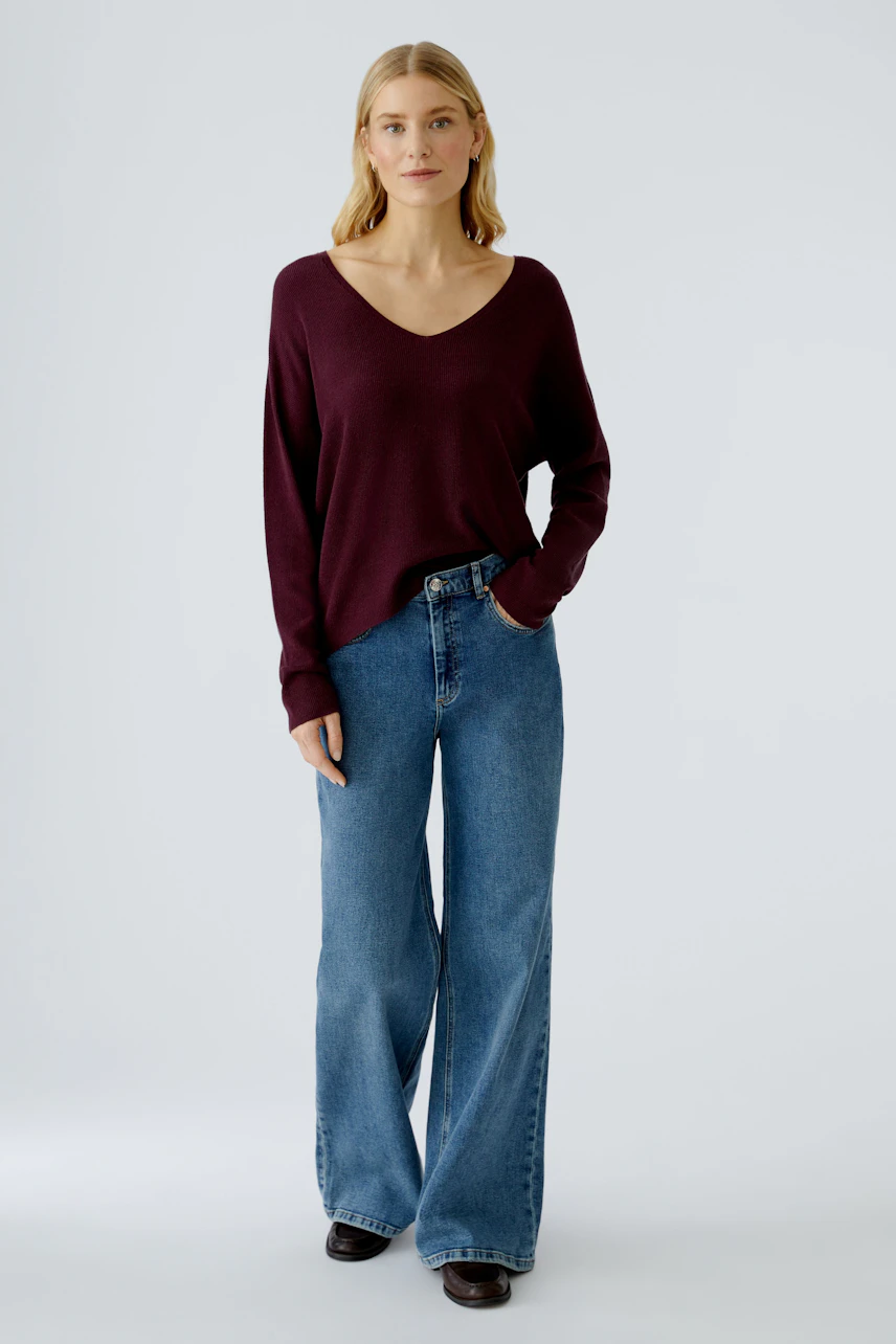 Casual women's pullover: Young woman in a burgundy V-neck pullover paired with wide-leg jeans.