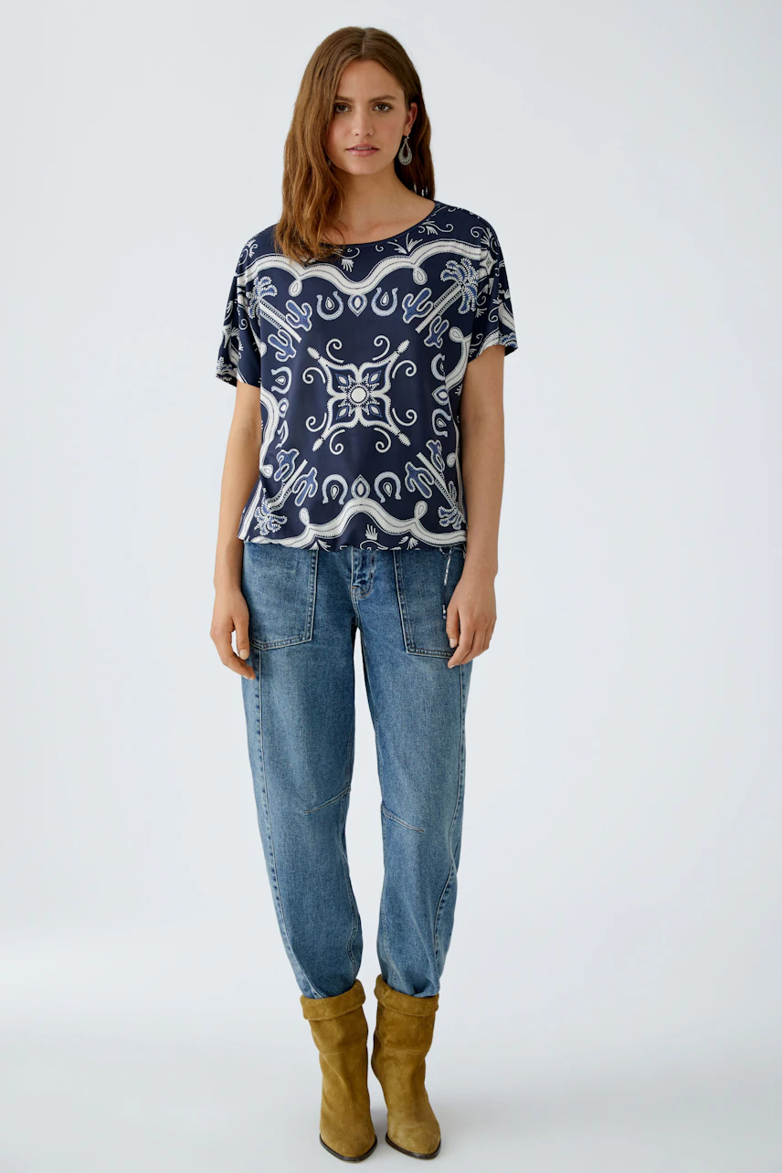Bequemes Damen-T-Shirt: Frau trägt ein navyfarbenes T-Shirt mit verspieltem Muster und lockeren Jeans.