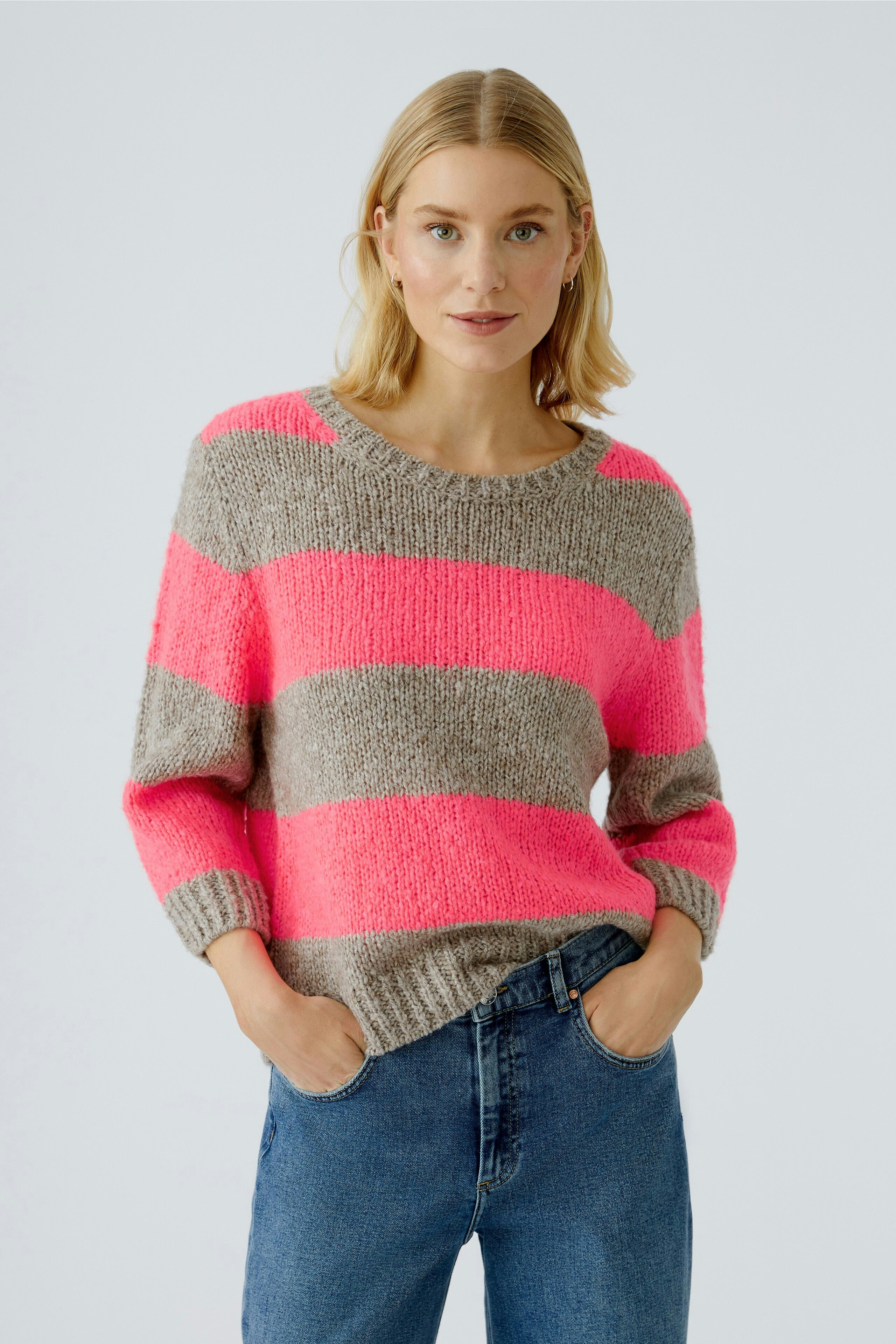 Casual women's pullover: A woman in a striped pullover with pink and gray colors, paired with jeans.