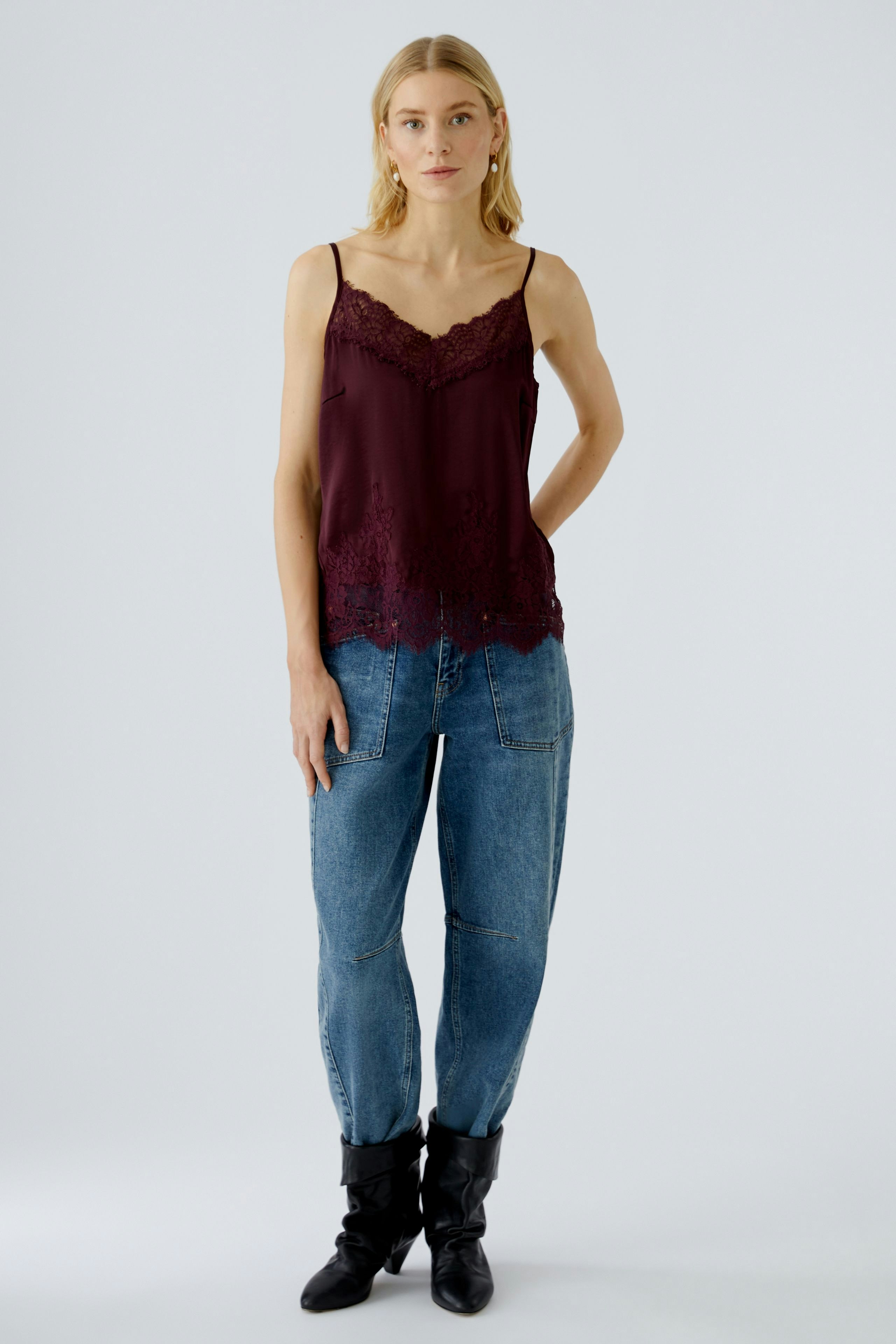 Casual women's top: Young woman in a burgundy lace-trimmed tank top paired with relaxed jeans.