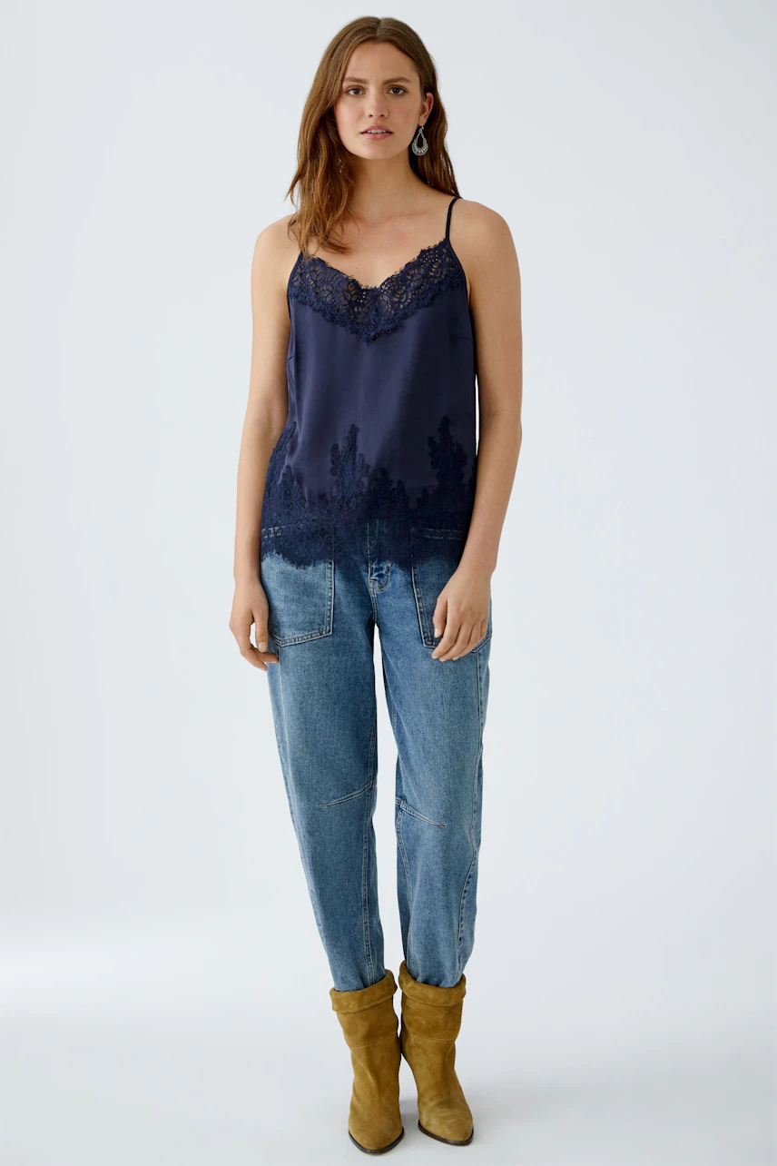 Casual women's top: Young woman in a navy lace-trimmed tank top paired with relaxed jeans.