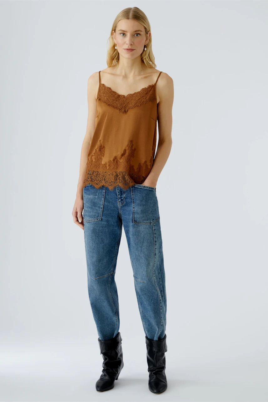 Casual women's top: Young woman in a brown lace-trimmed tank top paired with relaxed jeans.