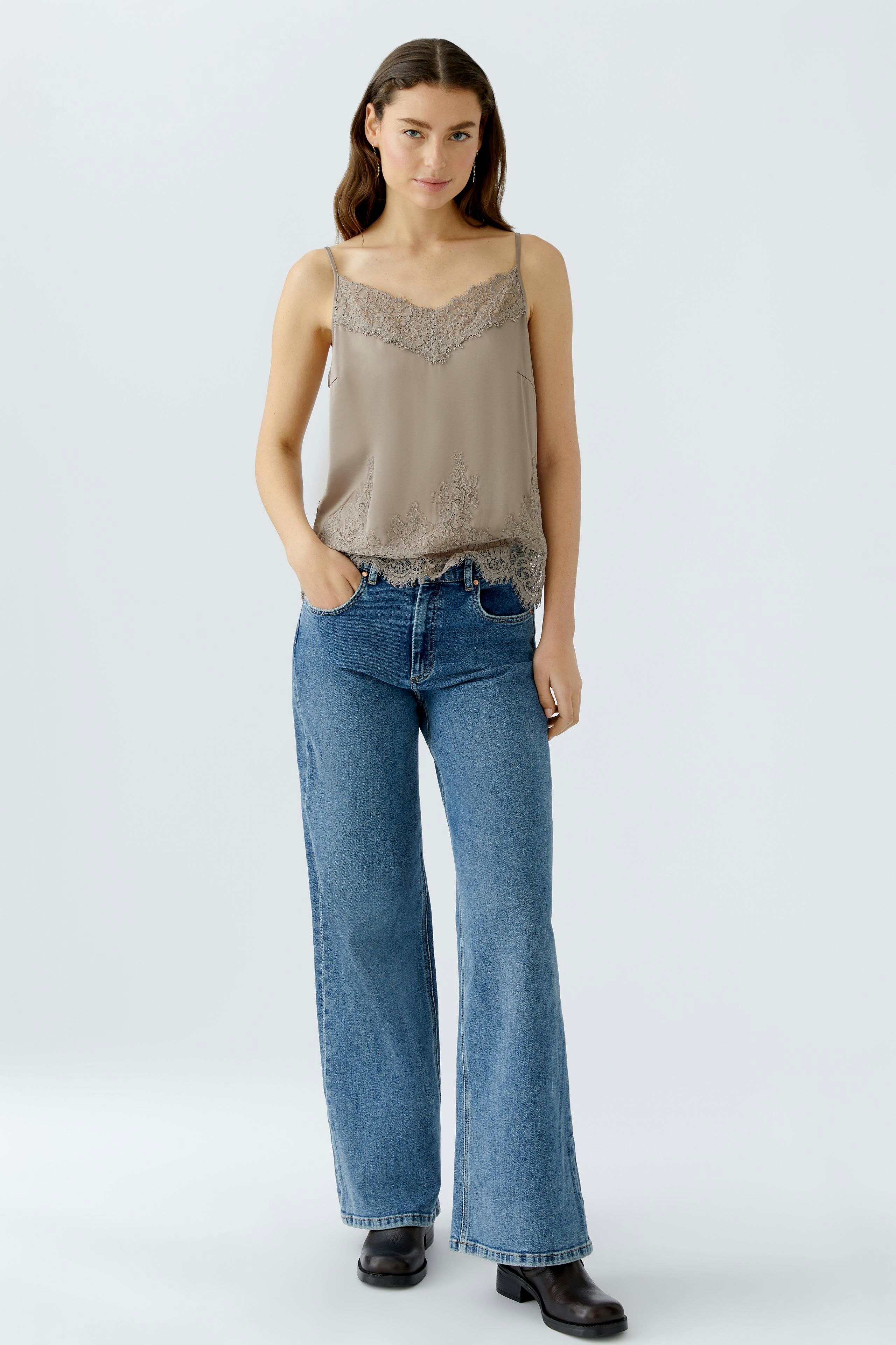Casual women's top: Young woman in a beige lace-trimmed tank top paired with wide-leg jeans.
