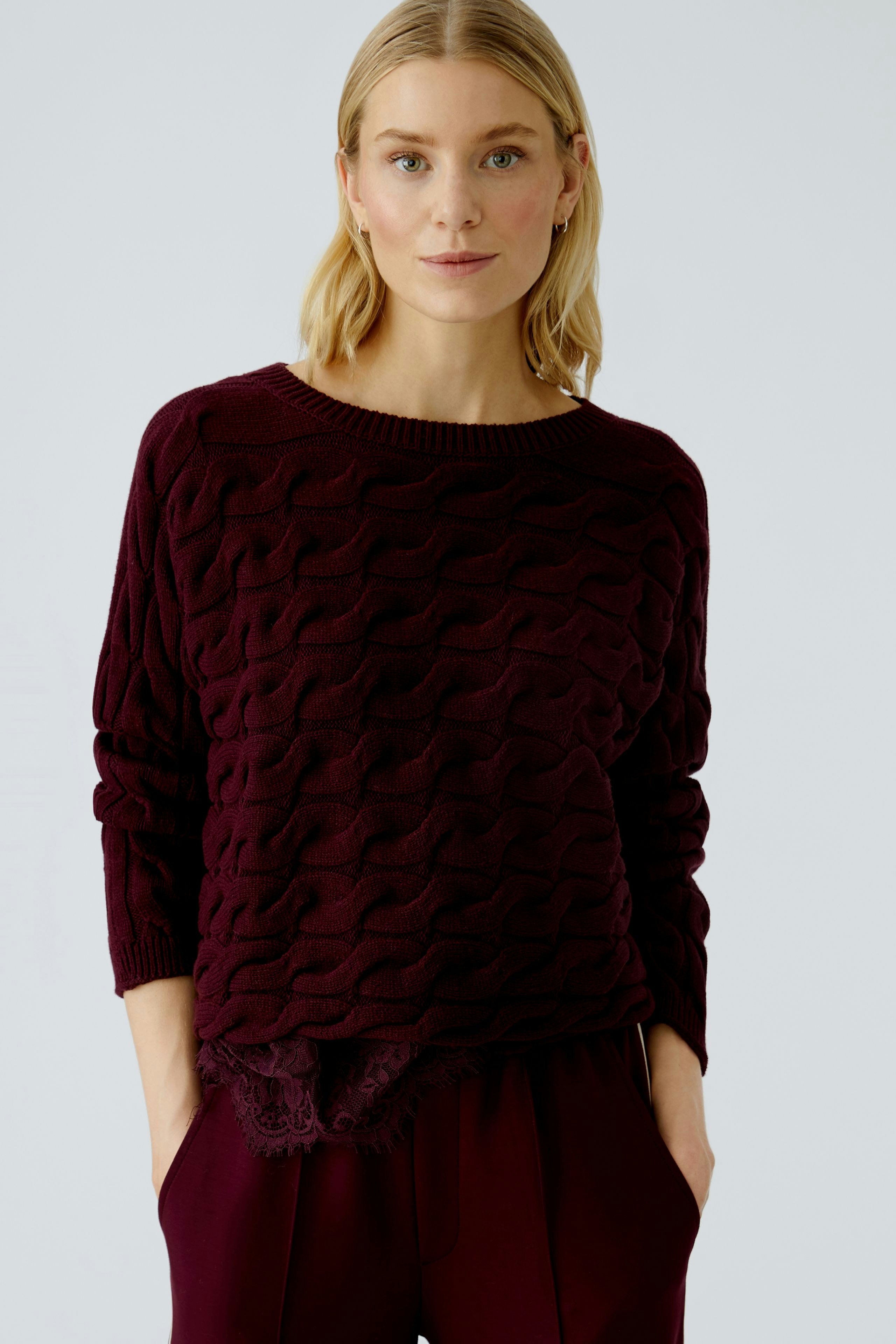 Casual women's pullover: A woman in a burgundy textured pullover with lace detail, looking relaxed.