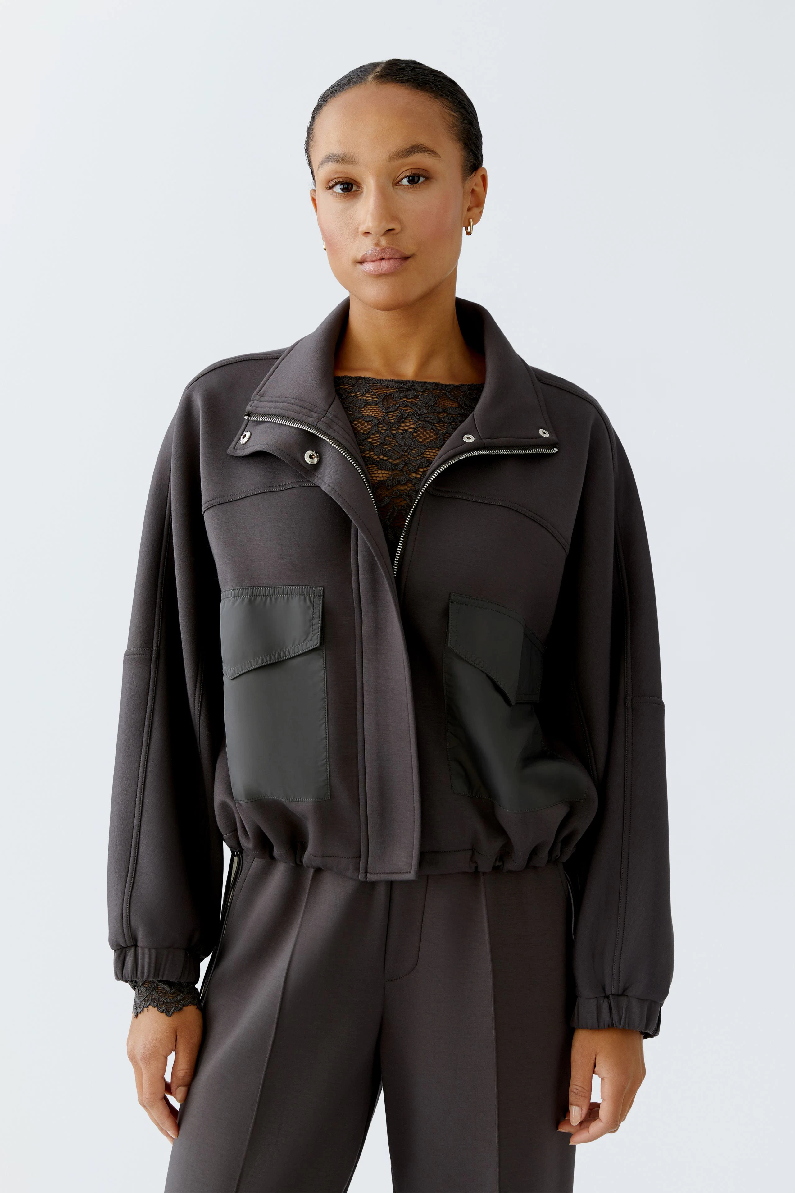 Casual women's jacket: A woman in a dark jacket with pockets, styled with a lace top and relaxed fit.