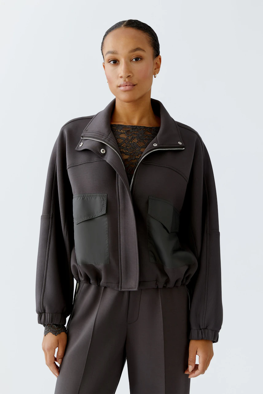 Casual women's jacket: A woman in a dark jacket with pockets, styled with a lace top and relaxed fit.