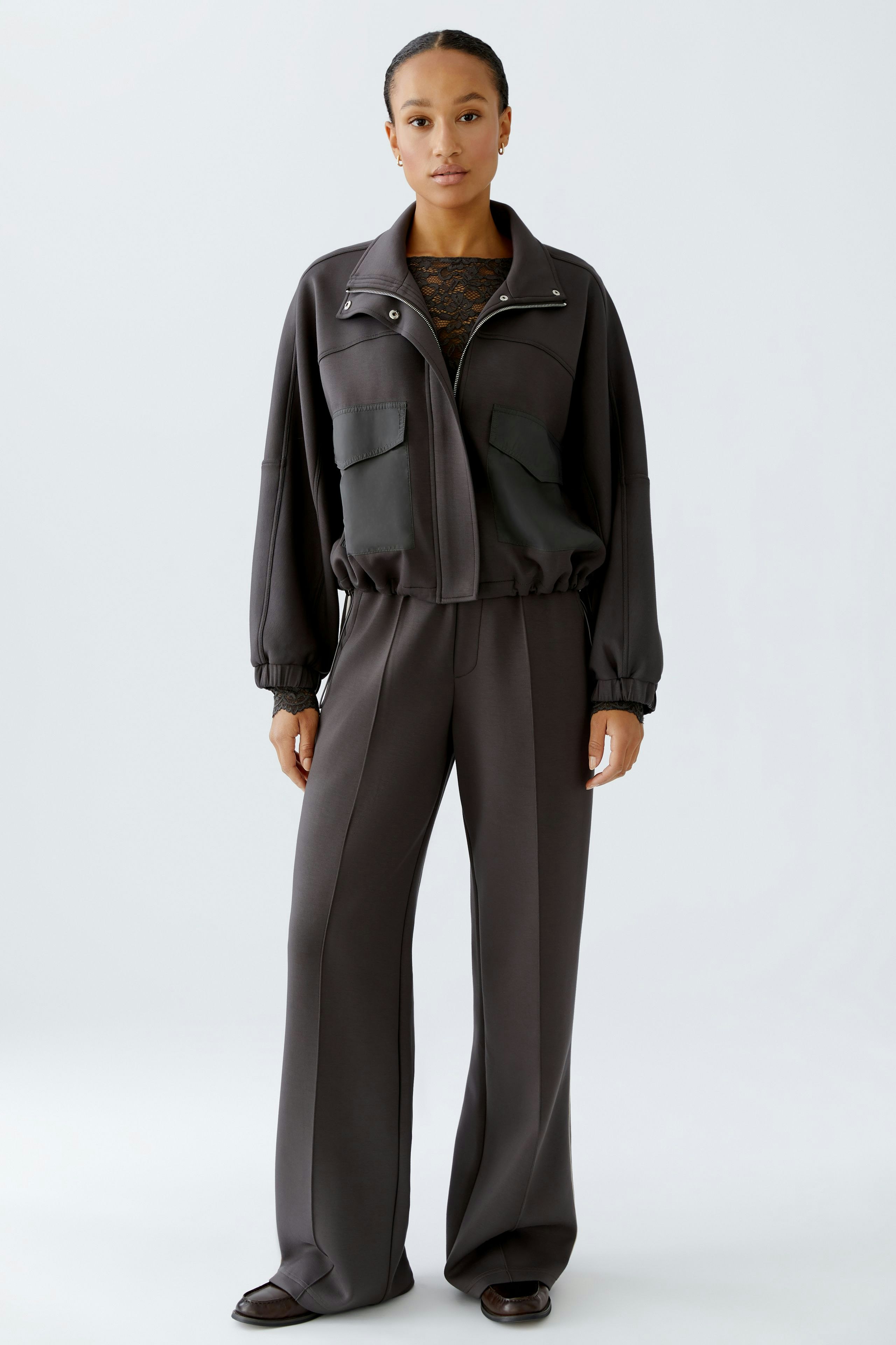 Casual women's jacket: A woman in a dark jacket with pockets and matching pants stands confidently.