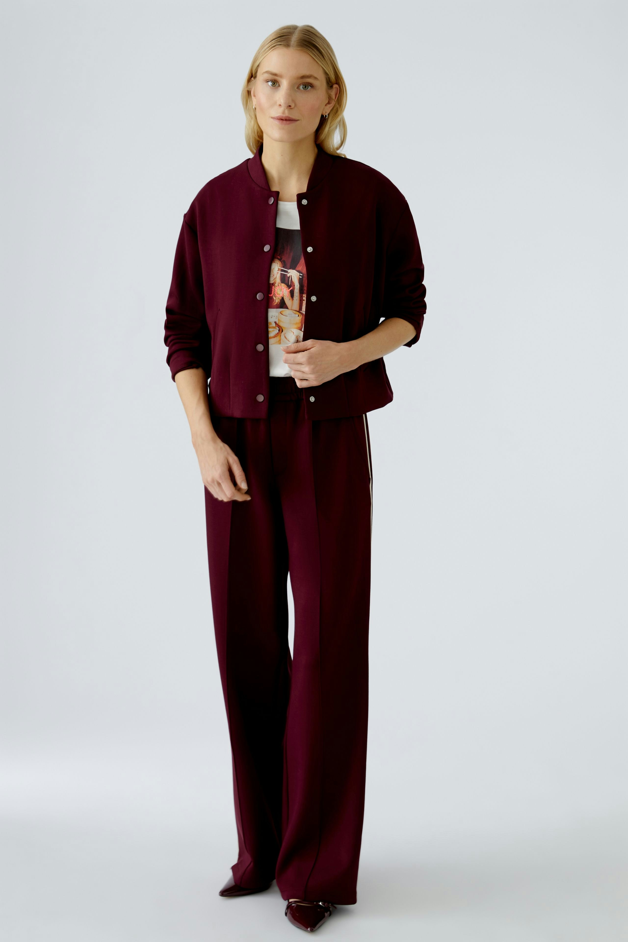 Damen-Blouson: Frau in bordeauxfarbener Bomberjacke mit Druckshirt und lässiger Hose.