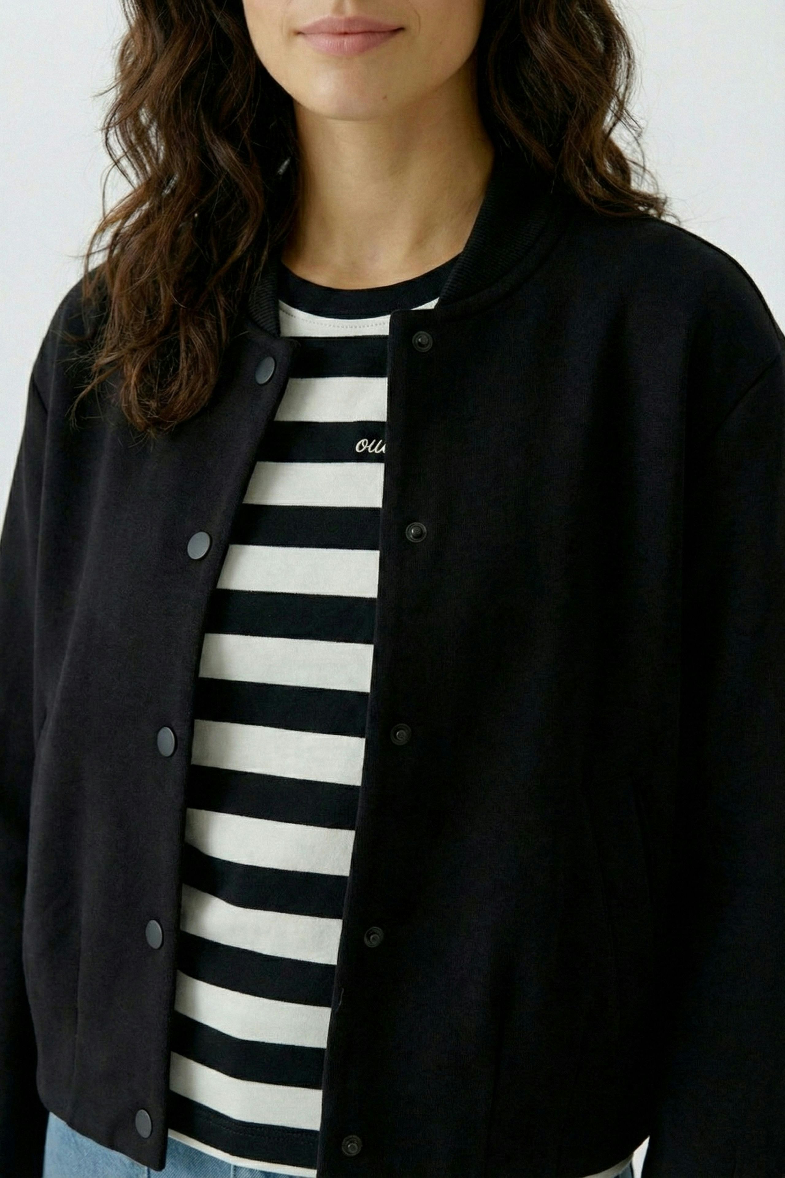 Damen-Bomberjacke: Frau in schwarzer Jacke über gestreiftem Shirt, lässiger Look.