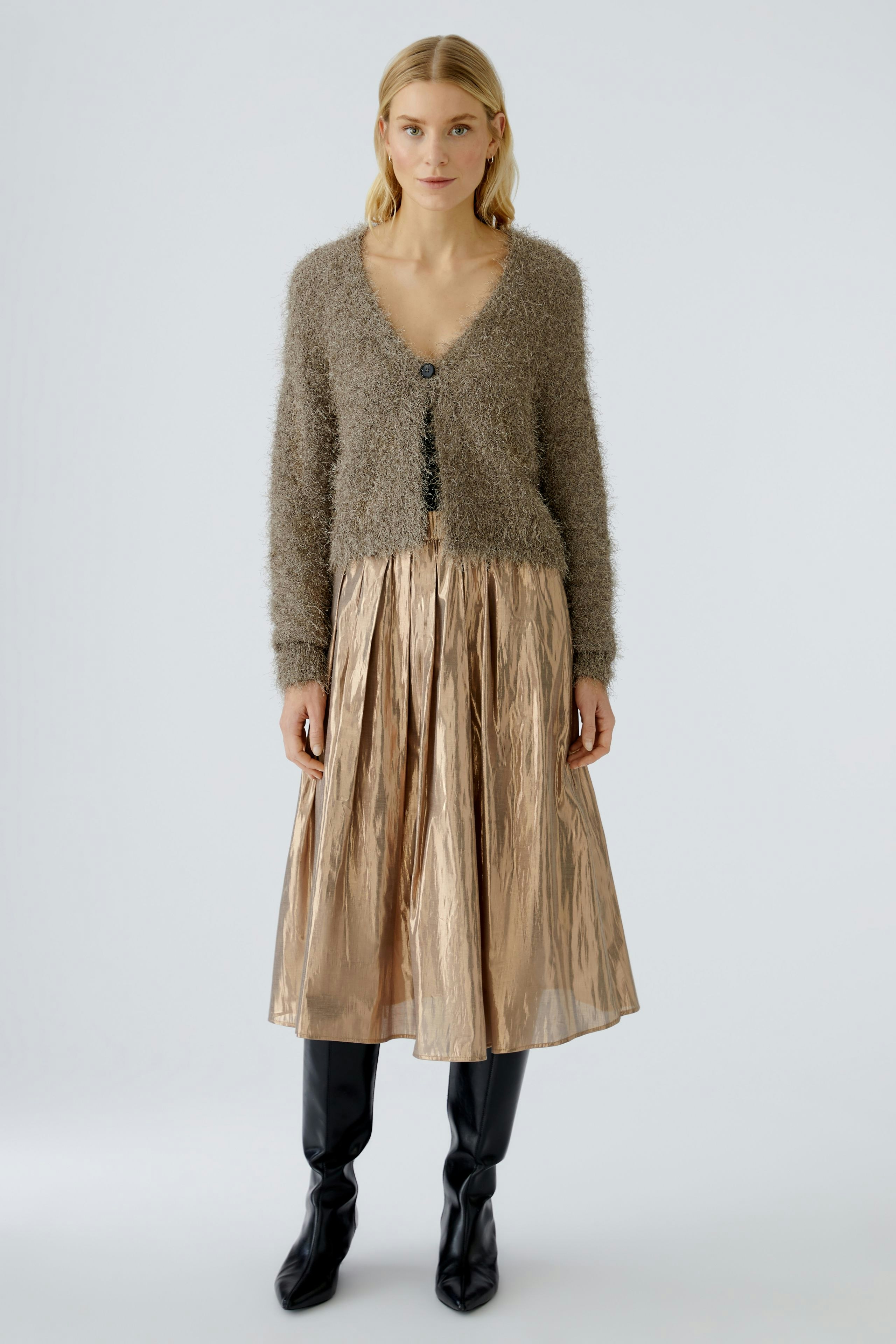 Bequeme Damen-Strickjacke: Frau in flauschiger, grauer Strickjacke mit Knöpfen und glänzendem Rock.