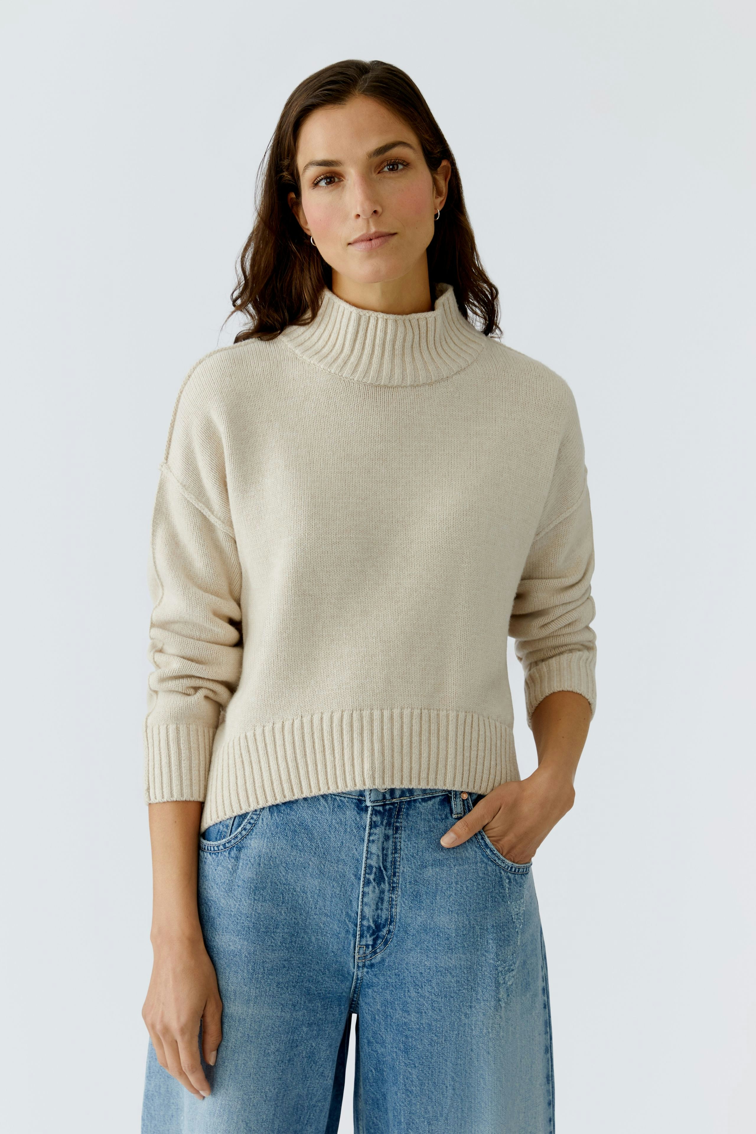 Casual women's pullover: A woman in a beige turtleneck pullover paired with wide jeans.