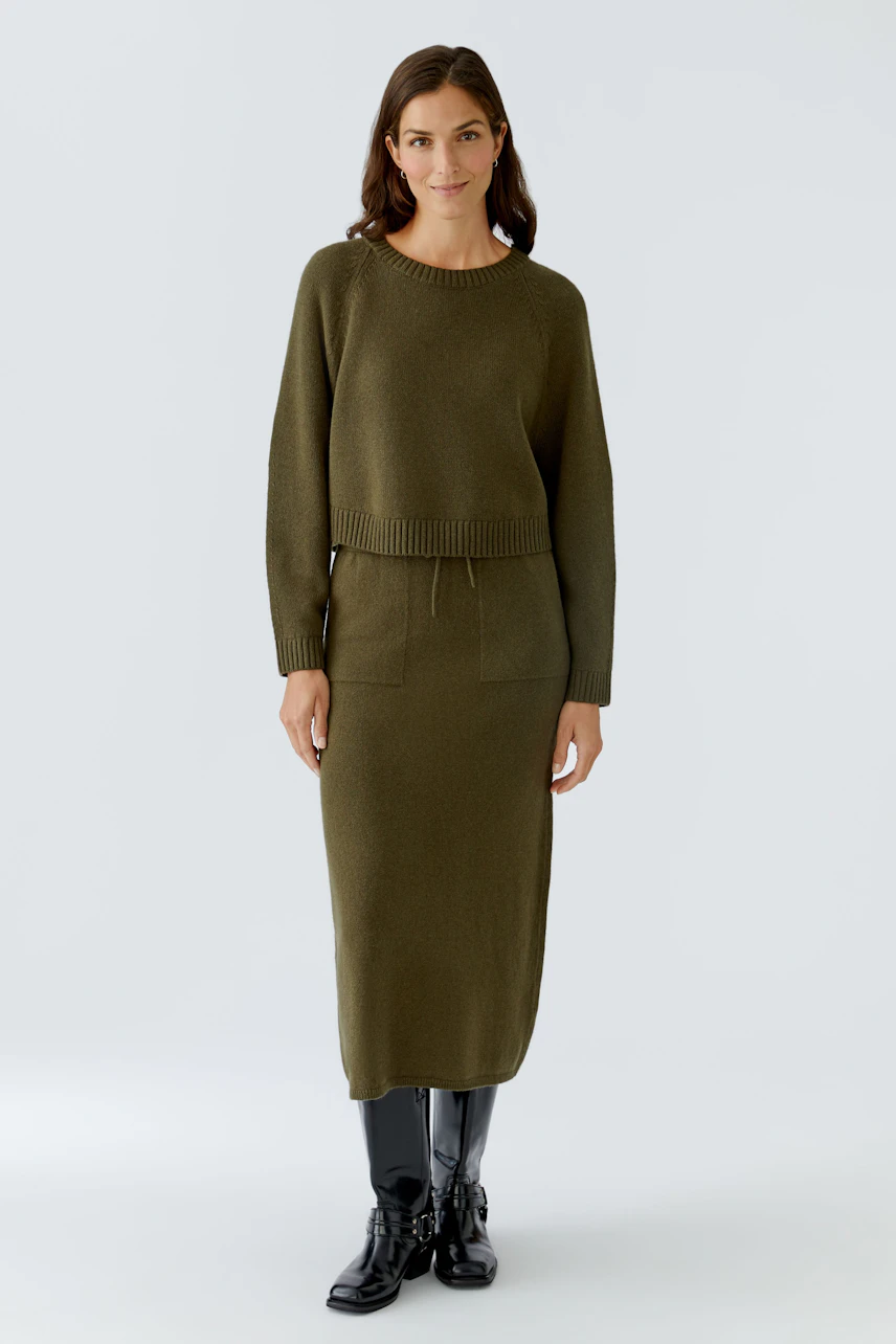 Casual women's pullover: A woman in an olive green pullover with a relaxed fit and ribbed hem.