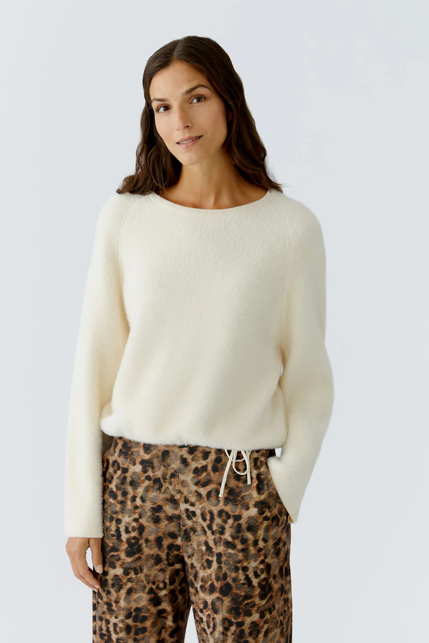 Damen-Pullover in Creme: Frau trägt einen weichen, lässigen Pullover mit Rundhalsausschnitt und lockerer Passform.