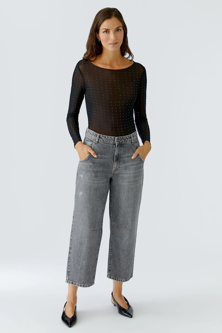 Long-sleeve shirt: Woman in a sheer black top with subtle dots, paired with relaxed-fit jeans.