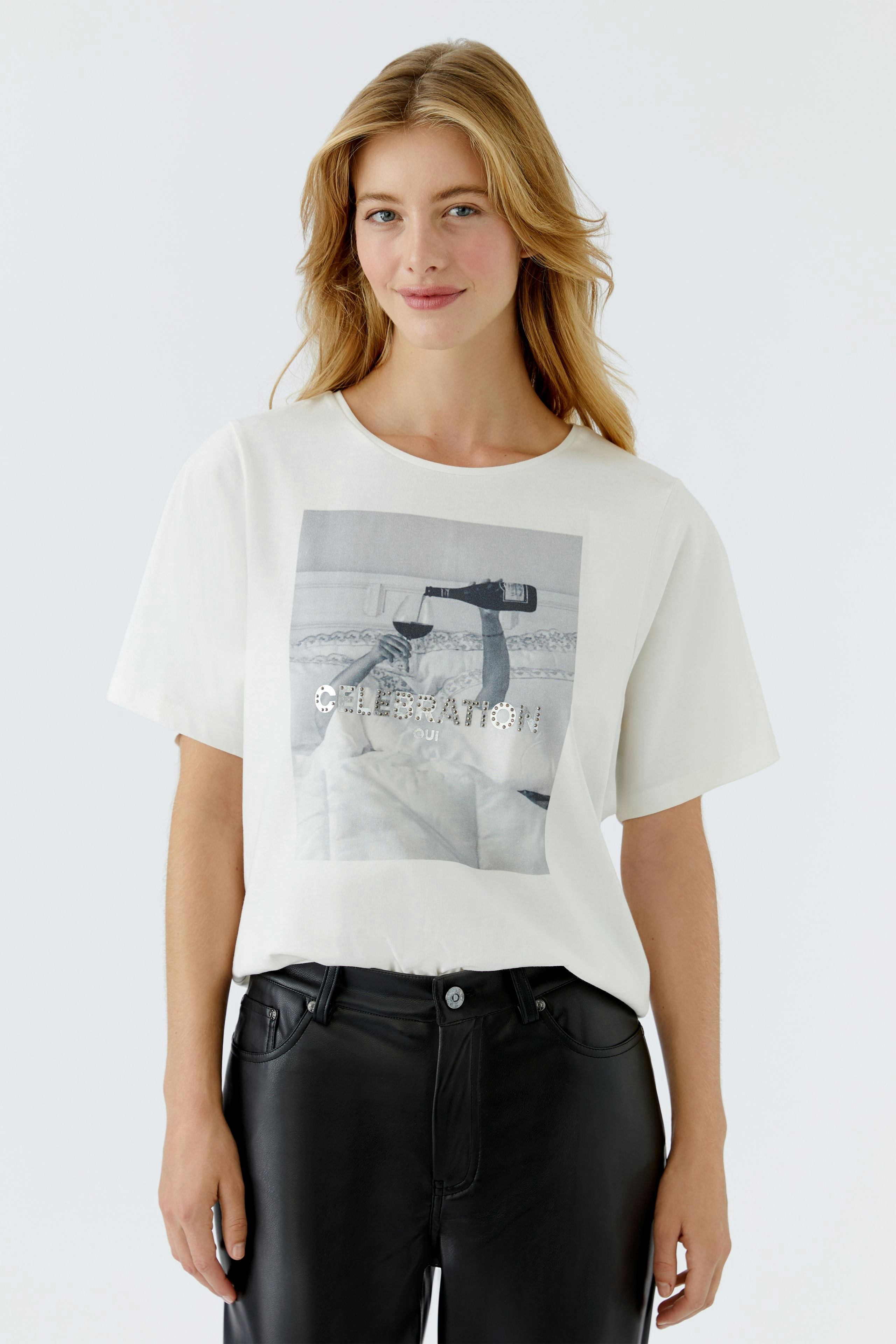 Bequeme Damen-T-Shirt: Frau trägt ein weißes T-Shirt mit grafischem Print und lässigen schwarzen Hosen.