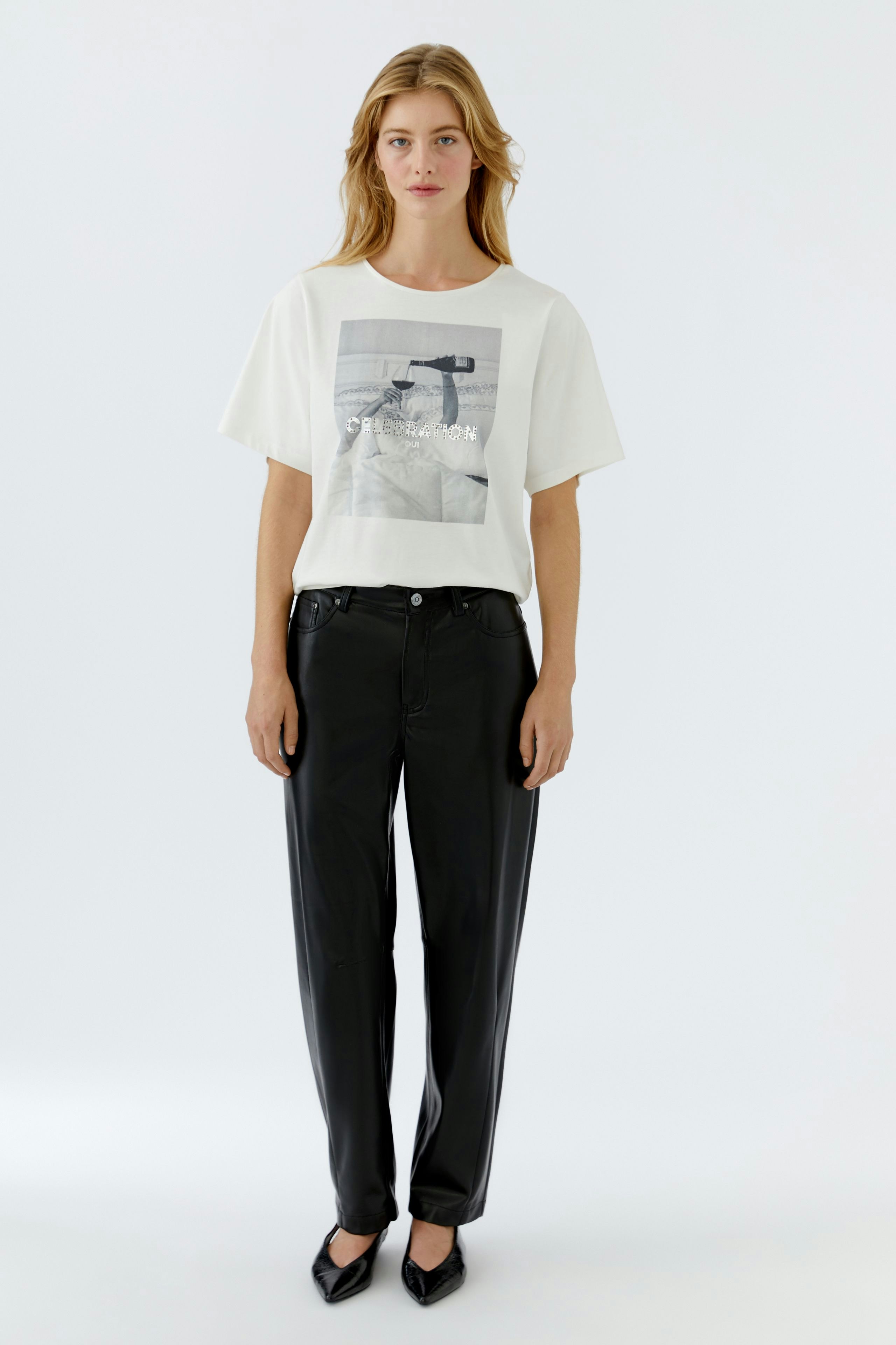 Bequeme Damen-T-Shirt: Frau trägt ein helles T-Shirt mit grafischem Print und lässigen schwarzen Hosen.