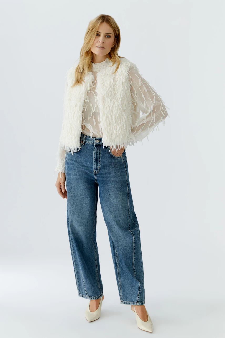 Faux fur vest: Woman in a fluffy white vest over a sheer top and wide jeans.