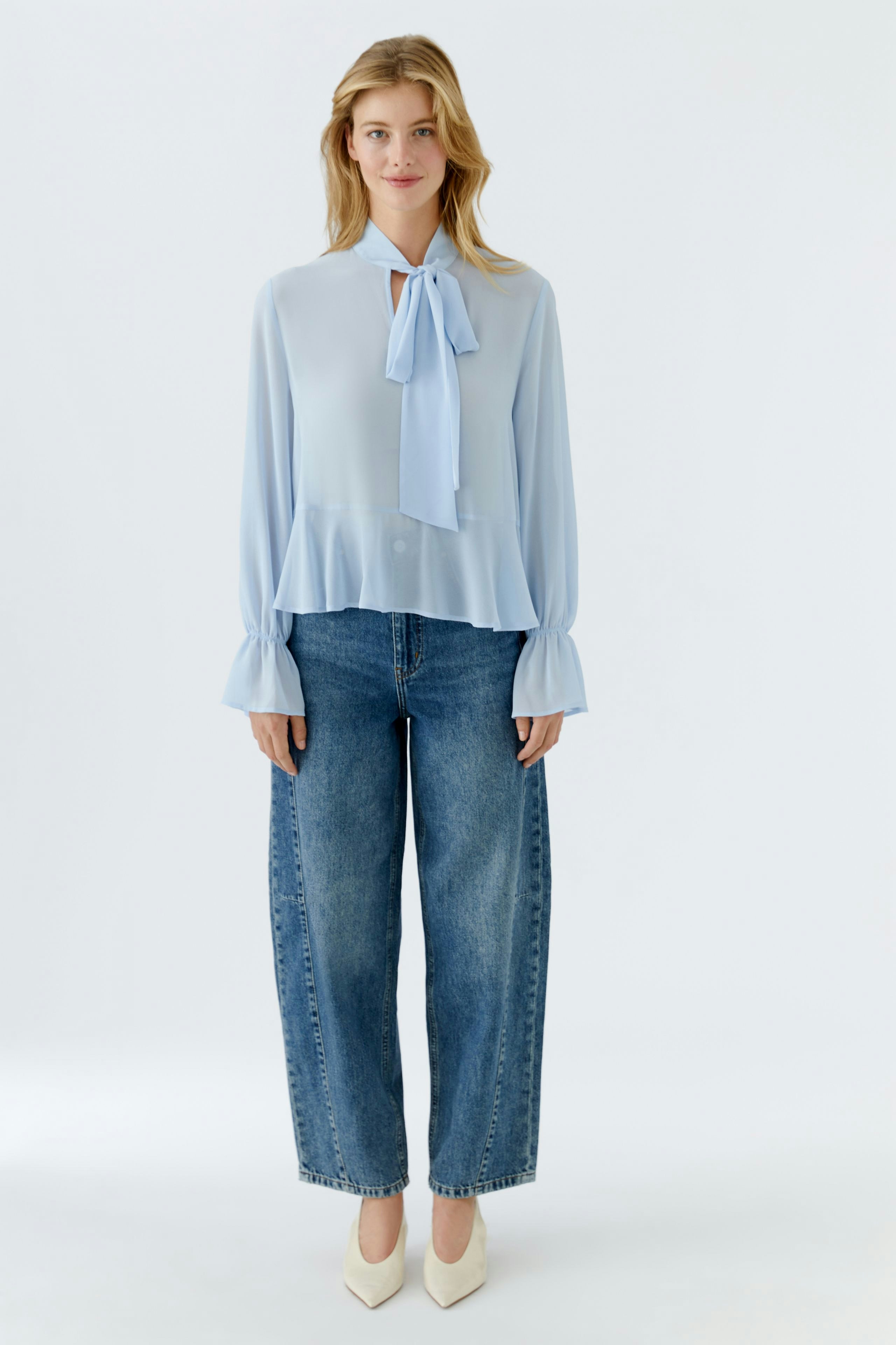Luftige Damen-Bluse in Hellblau mit Schleifenkragen, kombiniert mit lässigen Jeans.