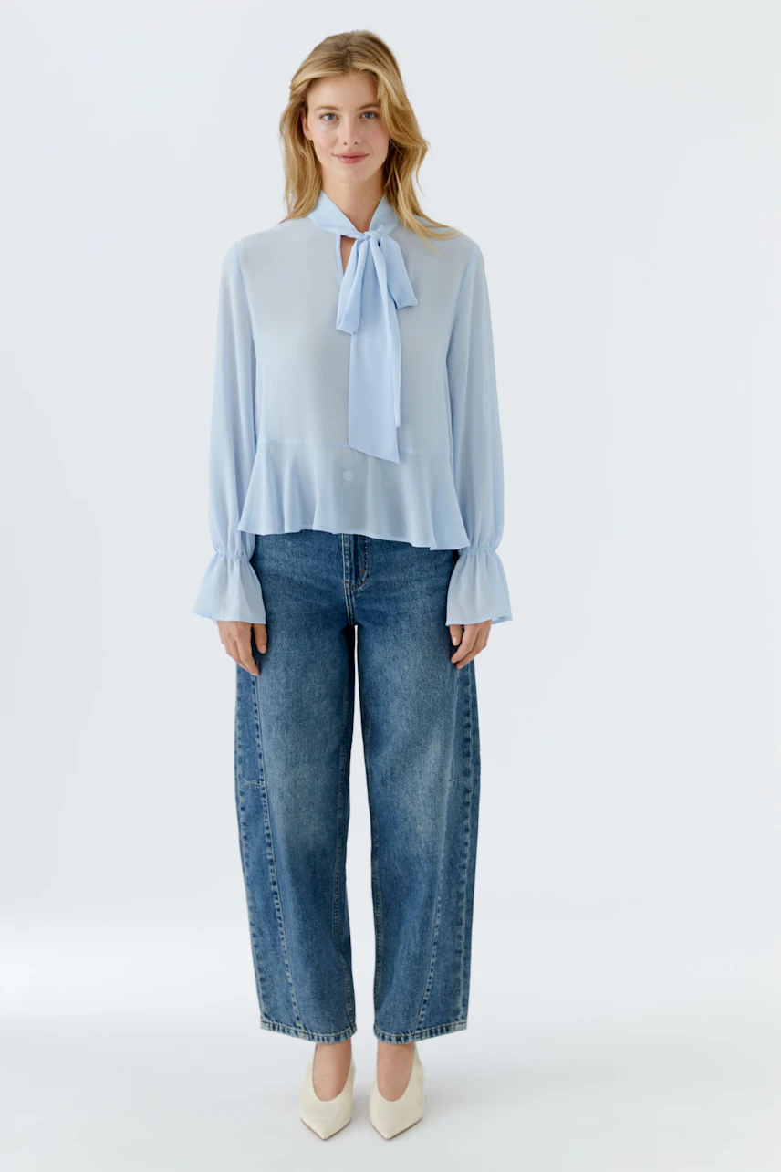 Luftige Damen-Bluse in Hellblau mit Schleifenkragen, kombiniert mit lässigen Jeans.