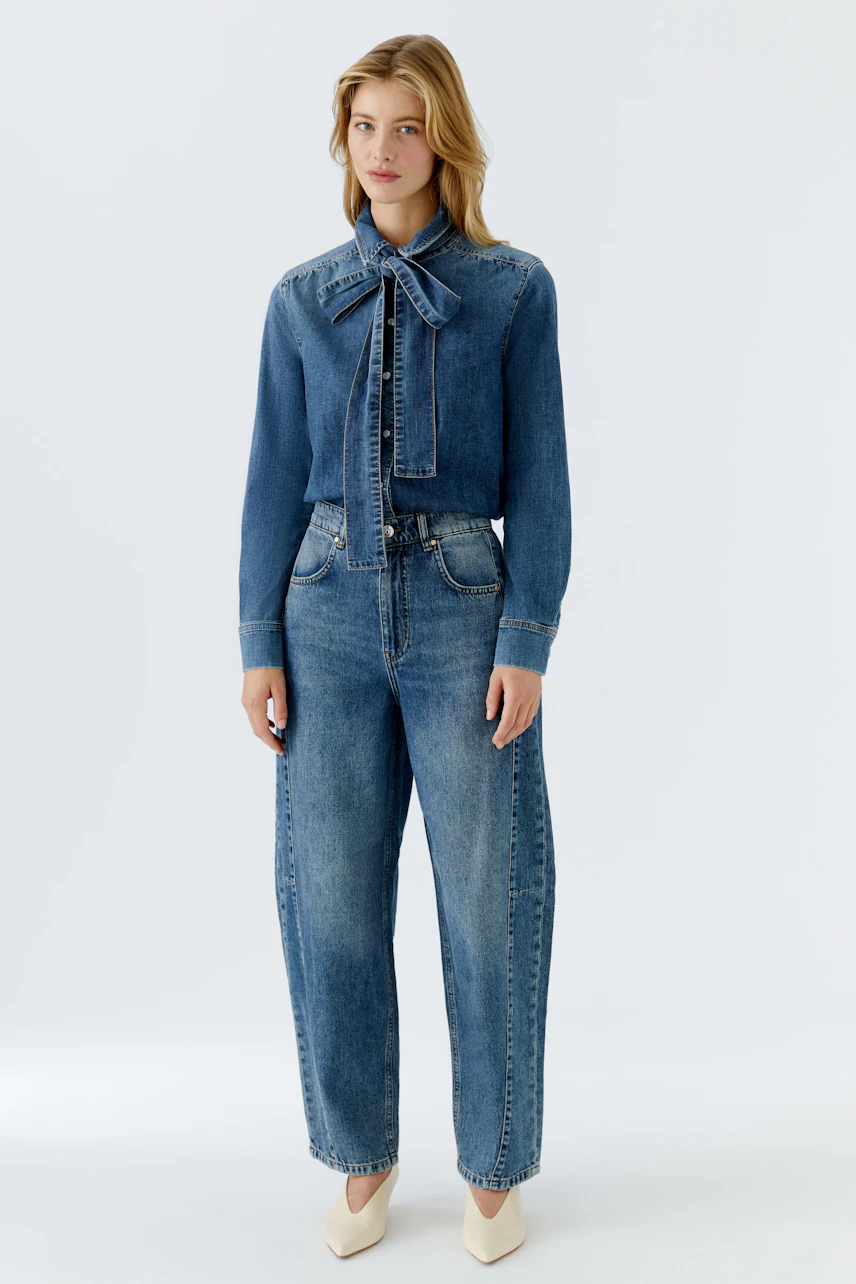 Damen-Jeanshemd: Frau in blauem Jeanshemd mit Schleife und lässigen Jeans steht selbstbewusst.