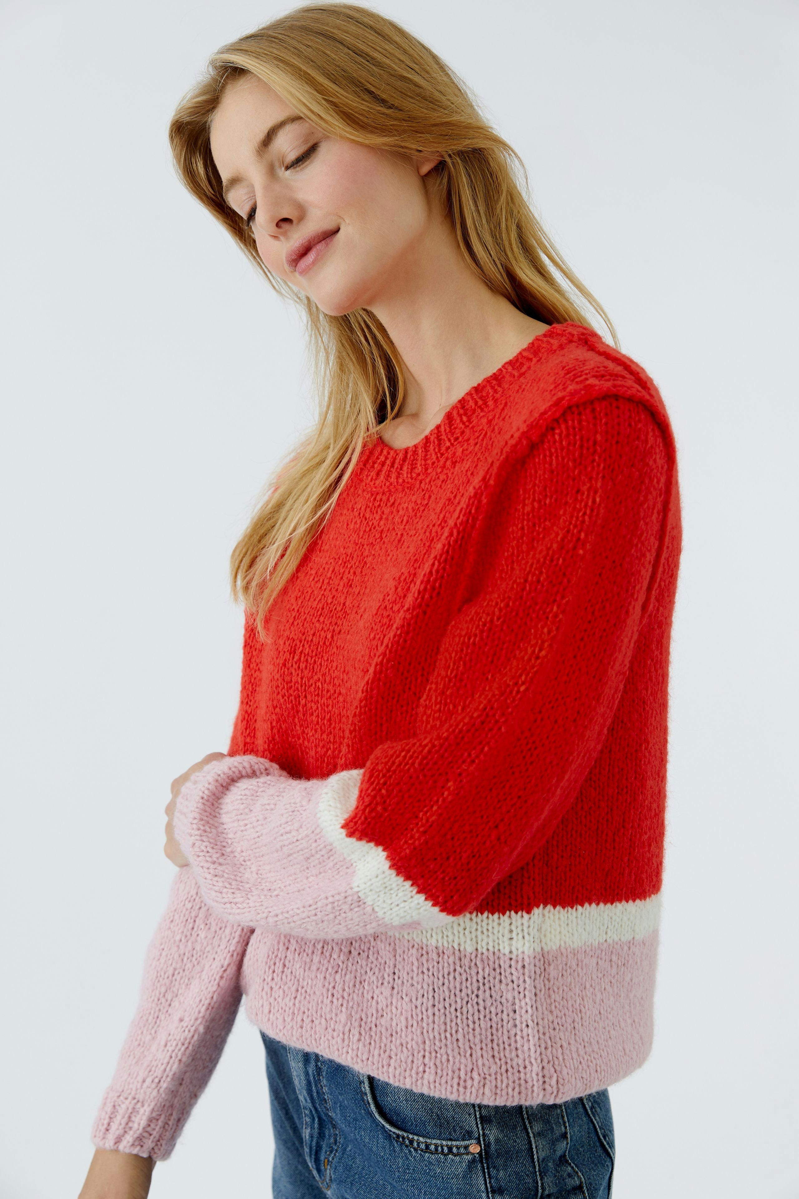 Casual women's pullover: Young woman in a red and pink knitted pullover with a relaxed fit.