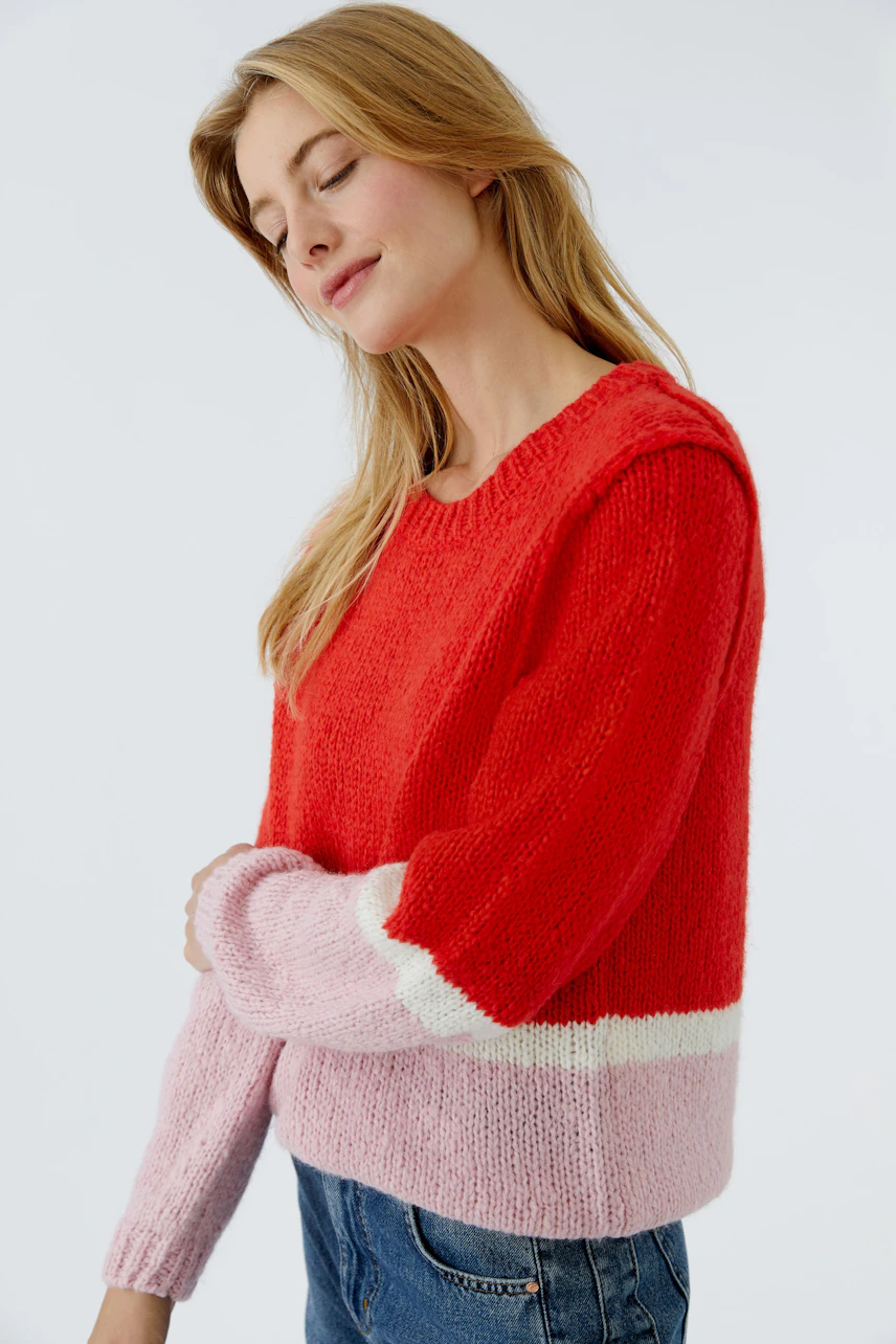 Casual women's pullover: Young woman in a red and pink knitted pullover with a relaxed fit.