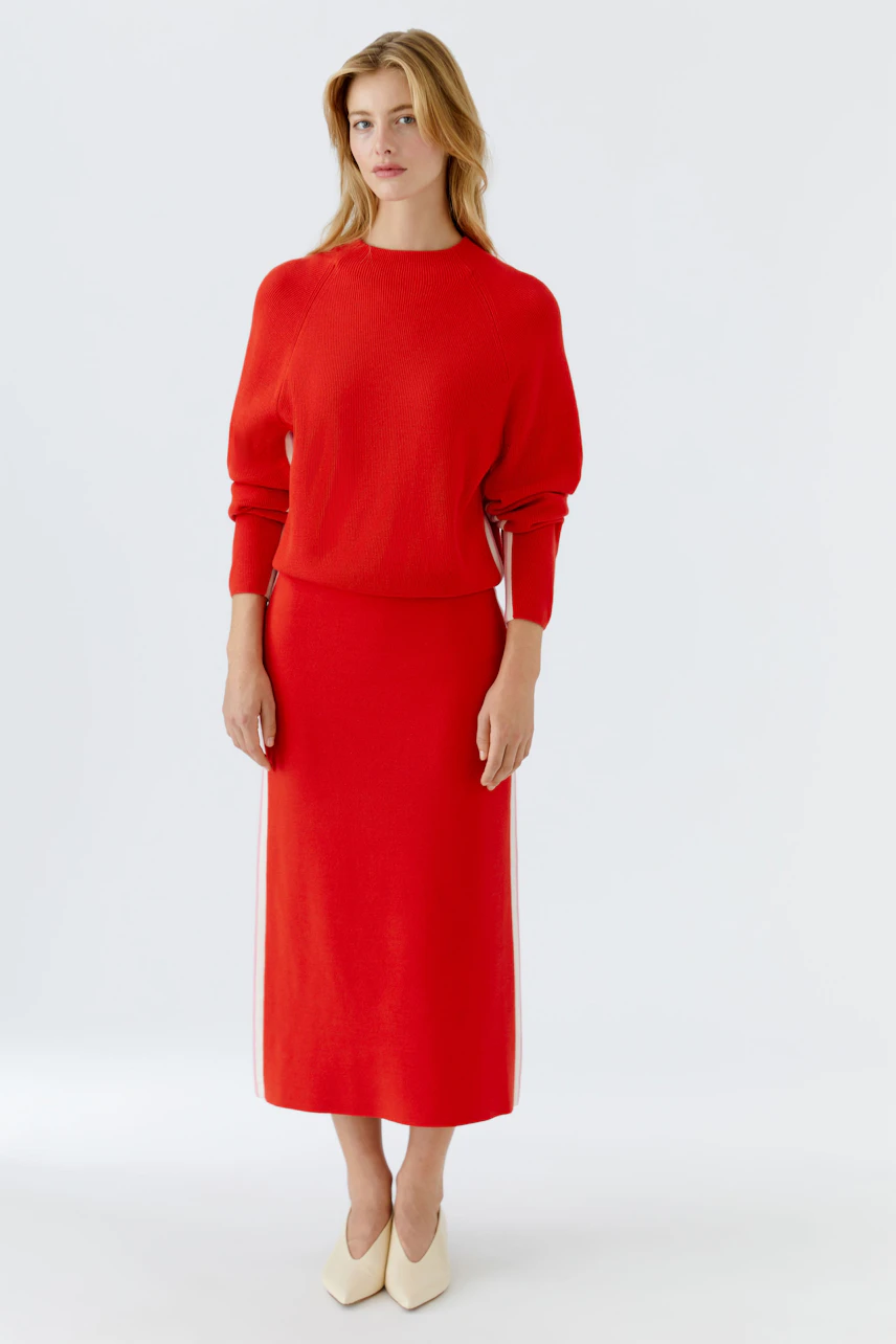 Modern women's pullover: A woman in a red pullover paired with a matching skirt, showcasing a relaxed style.