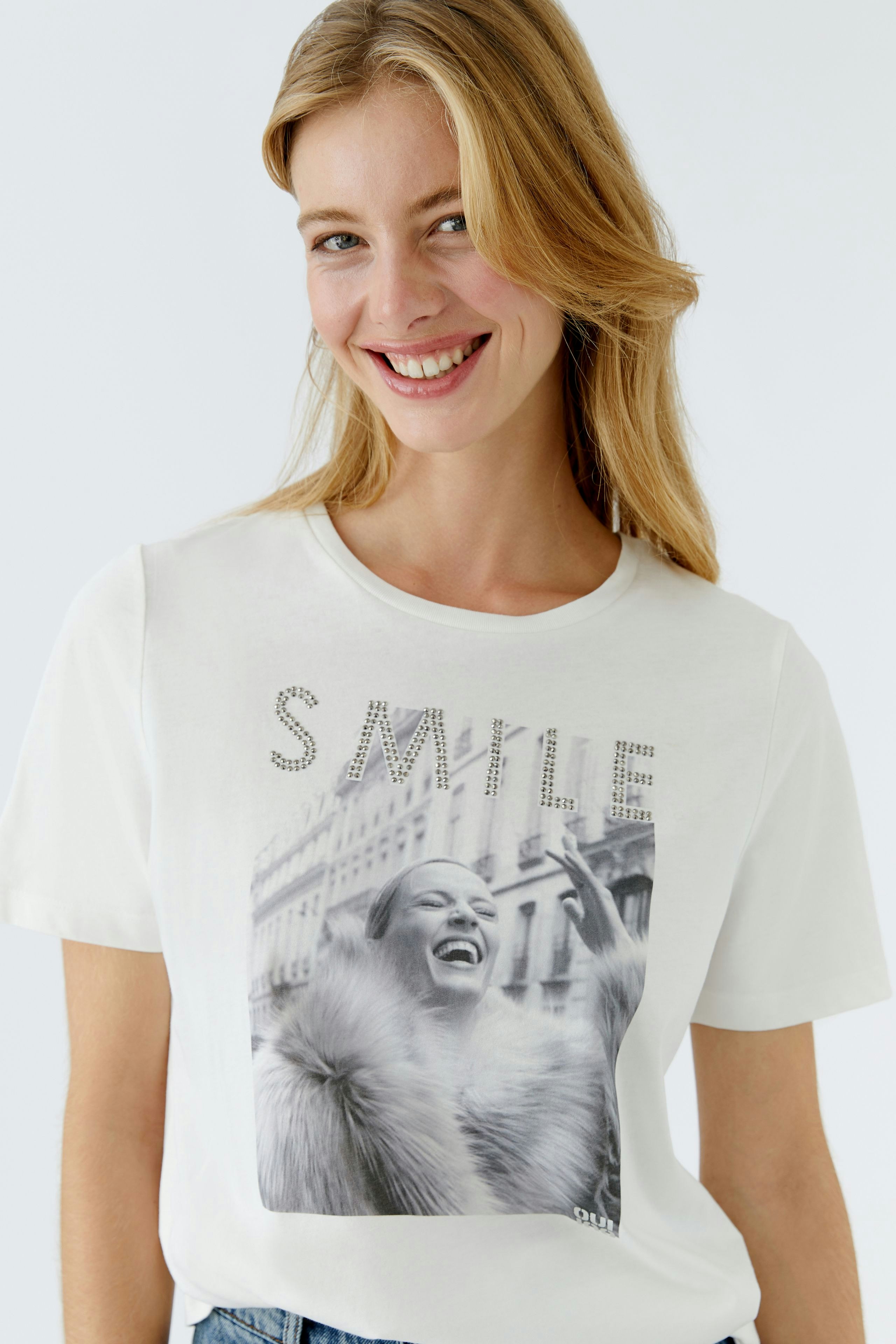 Casual women's T-shirt: Smiling woman in a white tee with a graphic print and relaxed fit.